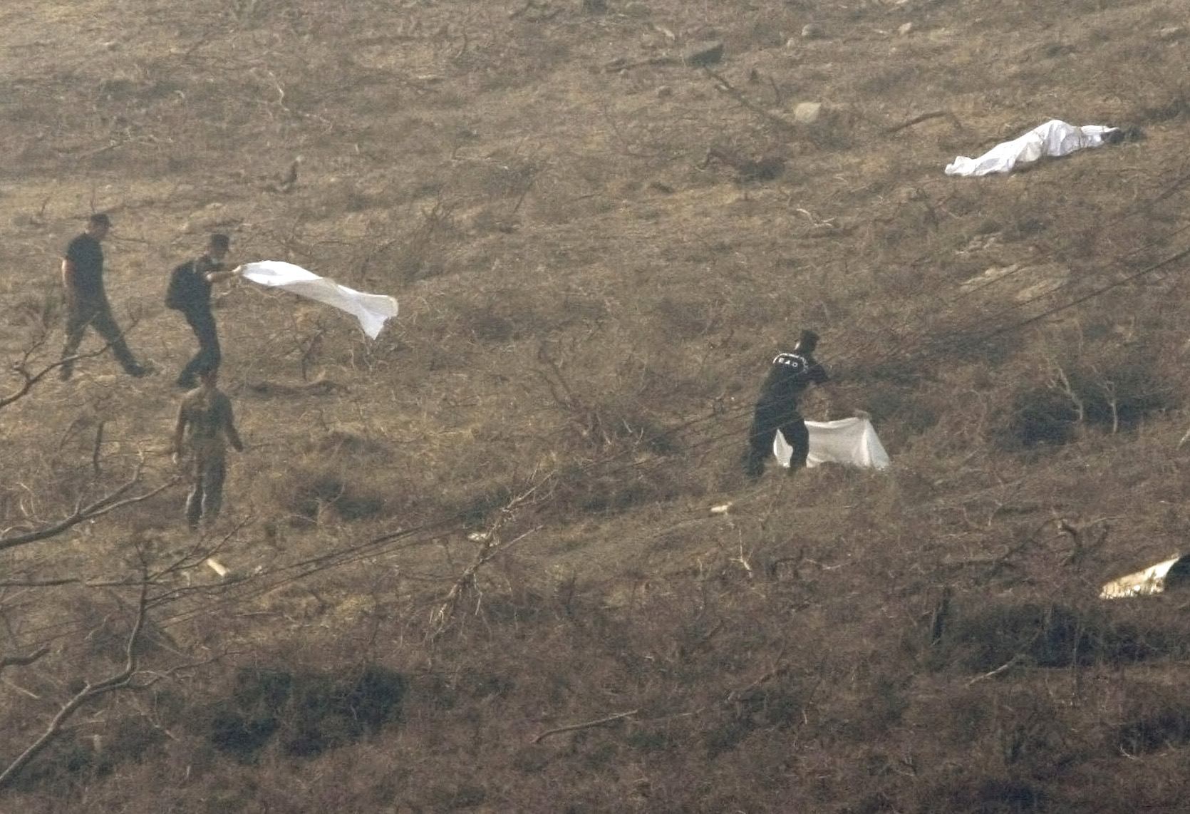 Άνδρες της ΕΜΑΚ σκεπάζουν πτώματα που έχουν εκσφενδονιστεί στο απέναντι βουνό. 