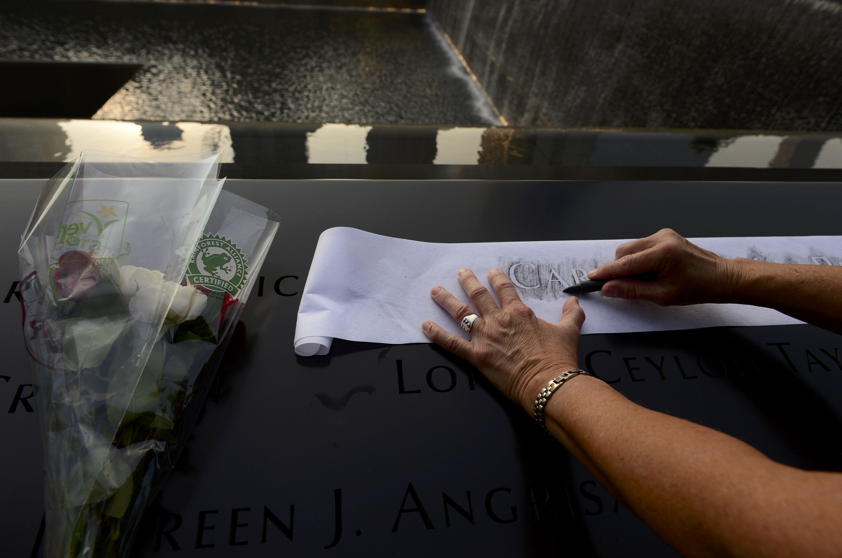Οι συγγενείς των θυμάτων κρατούν σε χαρτί τα ονόματα των αγαπημένων τους από το μνημείο