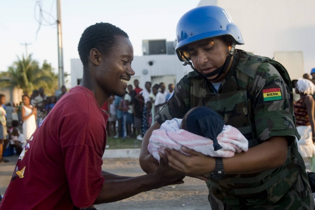 Ένας κυανόκρανος κρατάει ένα μωρό την ώρα που μοιράζεται φαγητό και νερό στους πληγέντες της Αϊτής ΦΩΤΟ REUTERS