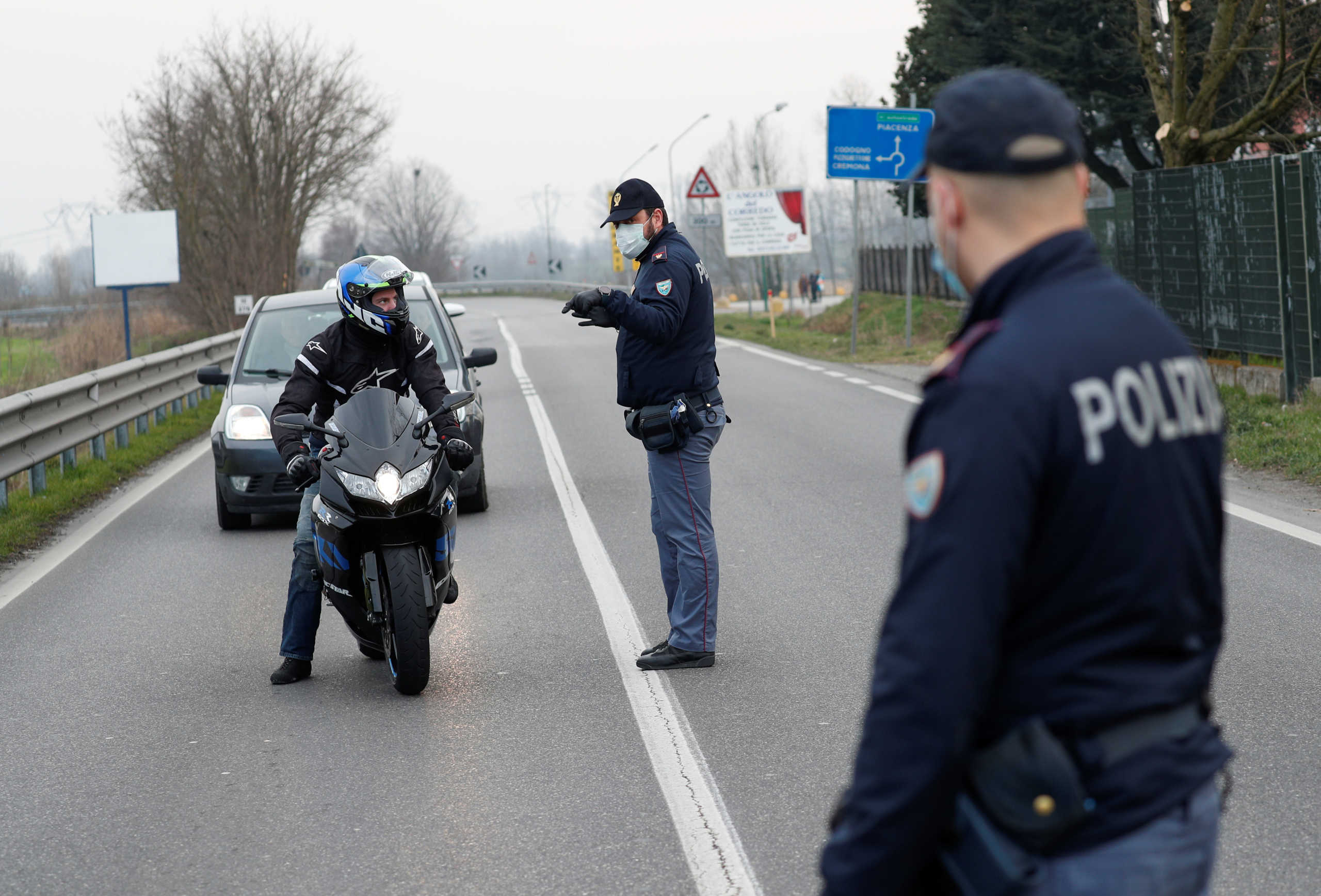 Policemen wearing face masks warn drivers on the road between Codogno and Casalpusterlengo, which has been closed by the Italian government due to a coronavirus outbreak in northern Italy, February 23, 2020. REUTERS