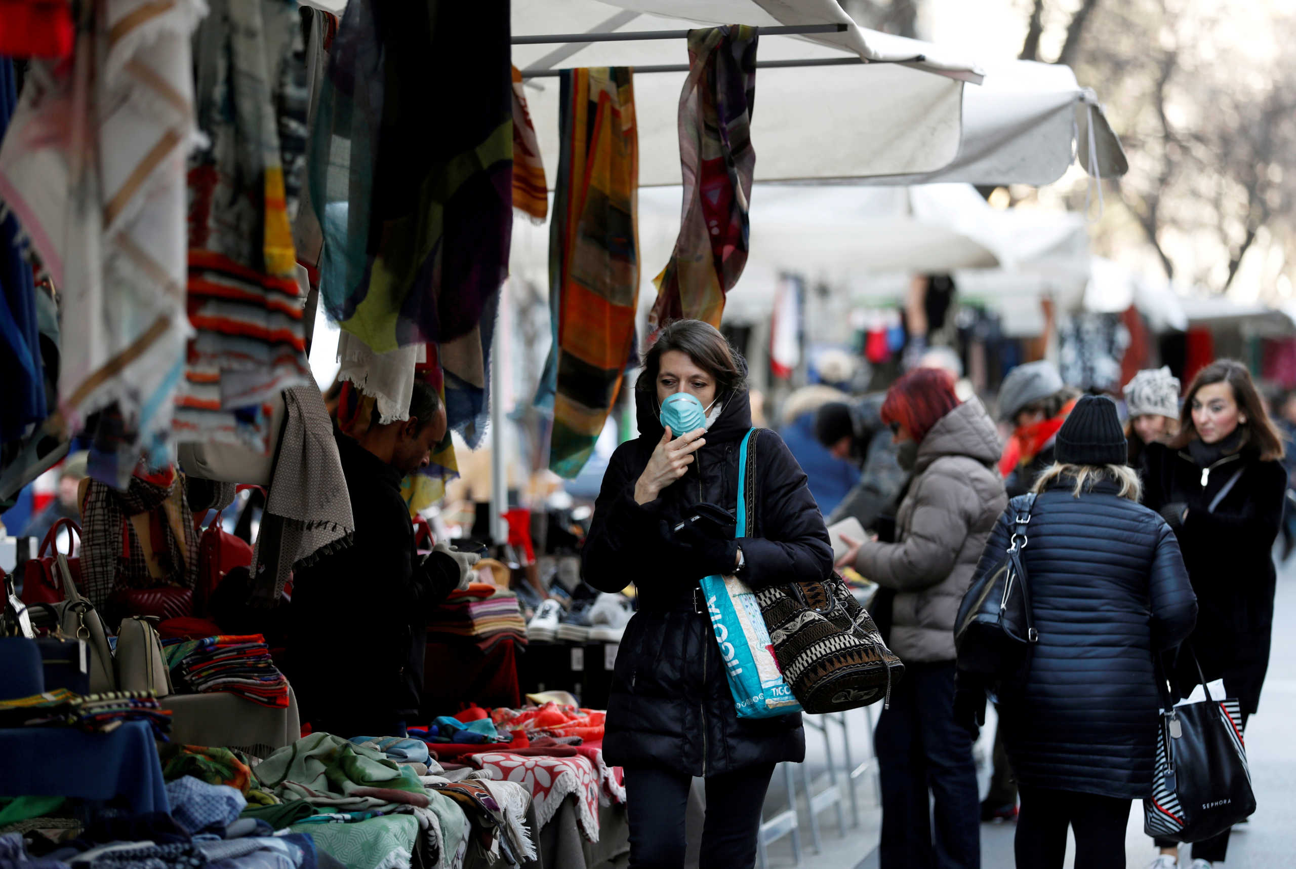 A woman wearing a protective face mask walks through a street market, as a coronavirus outbreak continues to grow in northern Italy, in Milan, Italy, February 27, 2020. REUTERS