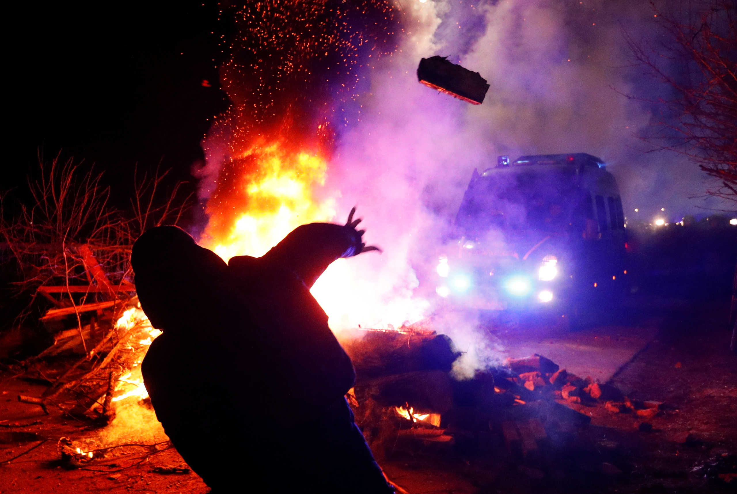 A demonstrator throws a stone towards a police van during a protest against the arrival of a plane carrying evacuees from coronavirus-hit China's Hubei province in the village of Novi Sanzhary in Poltava region, Ukraine February 20, 2020. Local residents blocked the road leading to a sanatorium where the evacuees are due to be held in quarantine for at least two weeks. REUTERS