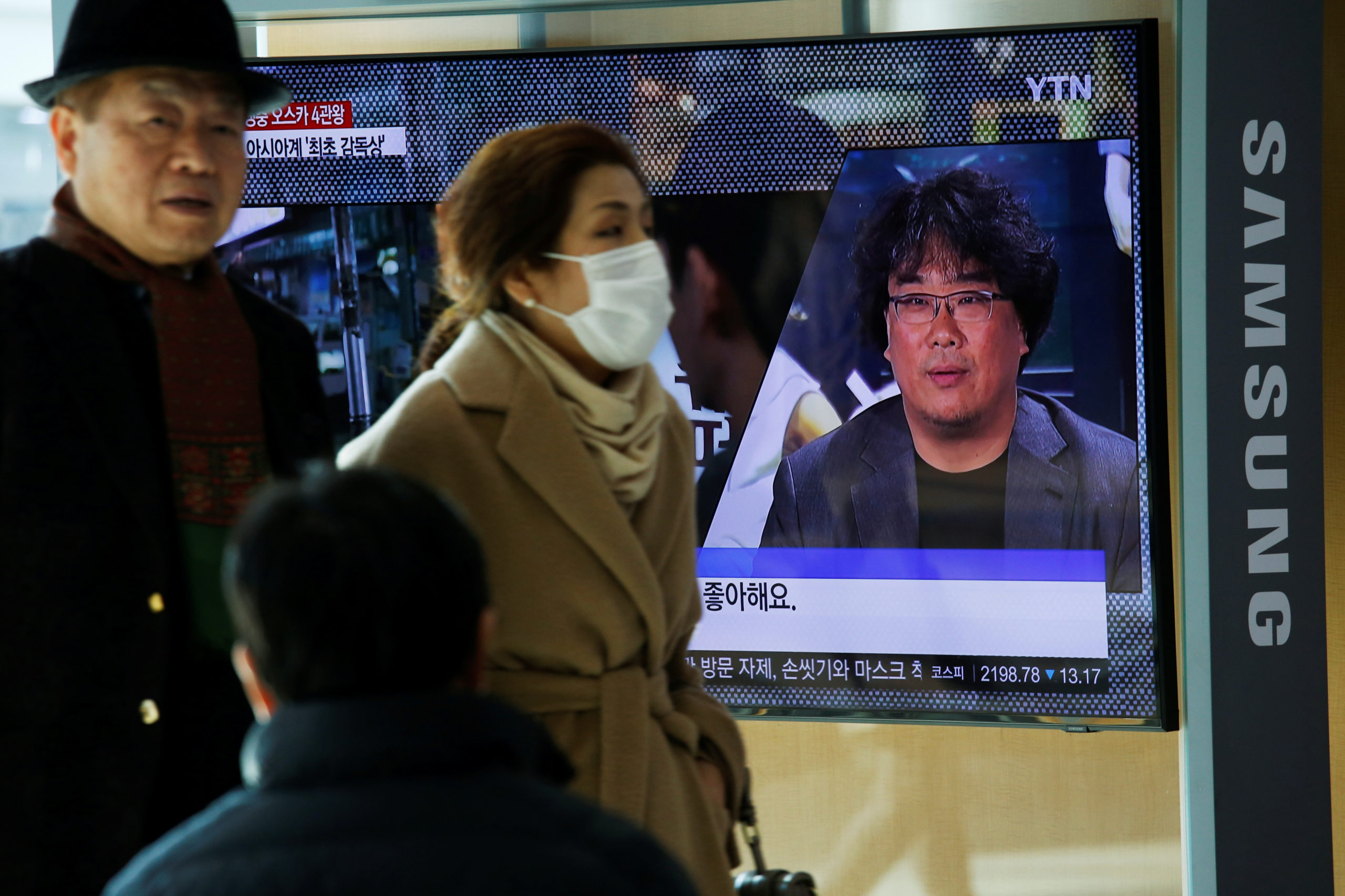 People watch a TV broadcasting a news report on South Korean director Bong Joon-ho who won four Oscars with his film "Parasite", in Seoul, South Korea, February 10, 2020.   REUTERS