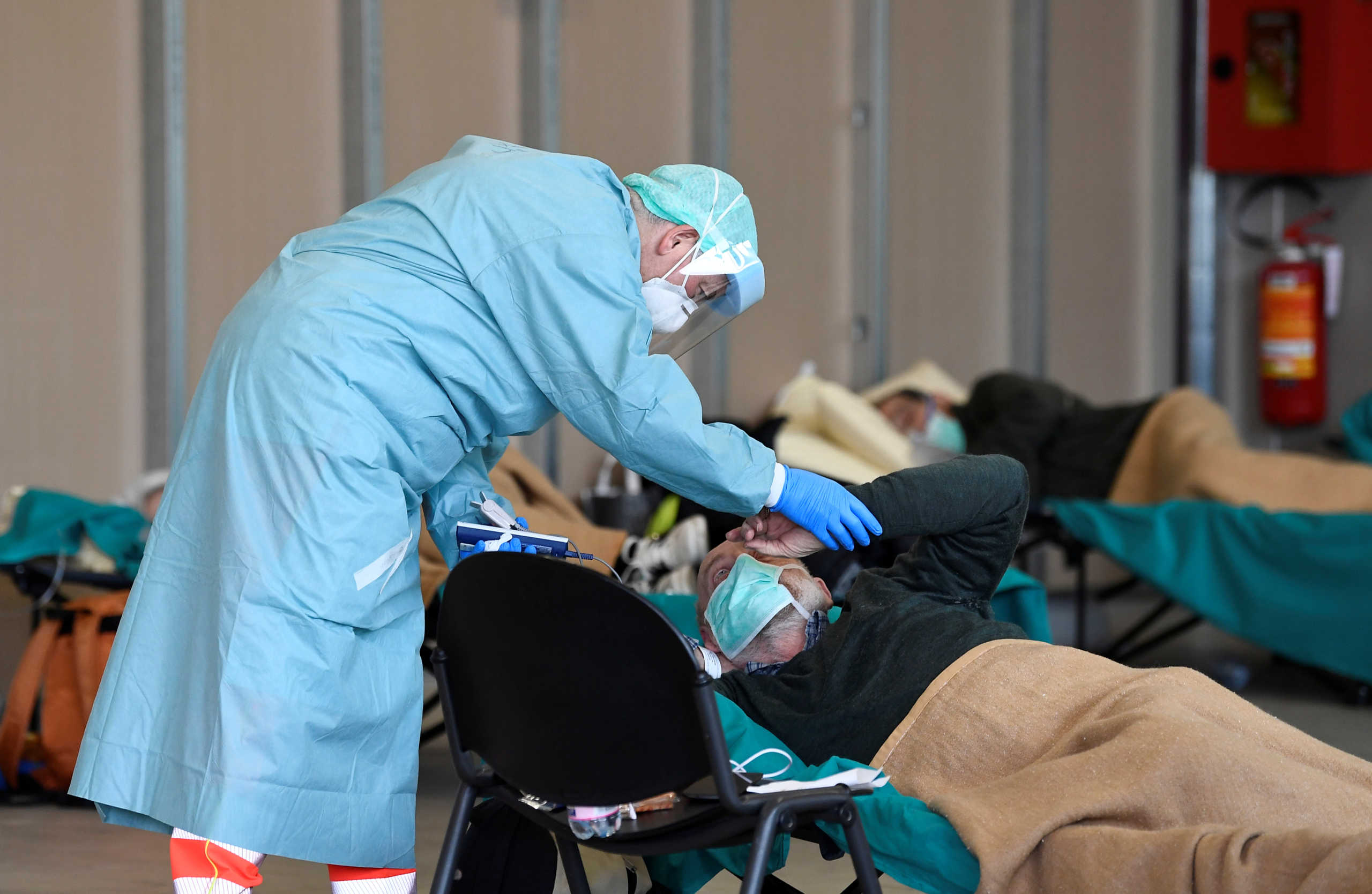 A member of the medical personnel wearing a protective face mask helps patients inside the Spedali Civili hospital in Brescia, Italy March 13, 2020. REUTERS