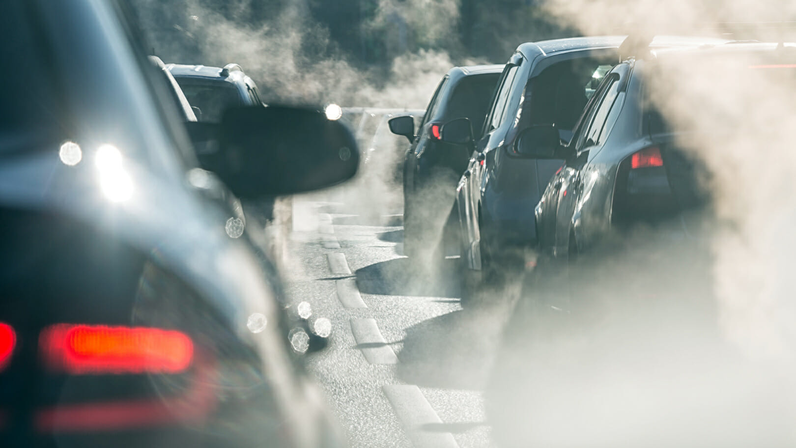 Blurred silhouettes of cars surrounded by steam from the exhaust pipes. Traffic jam