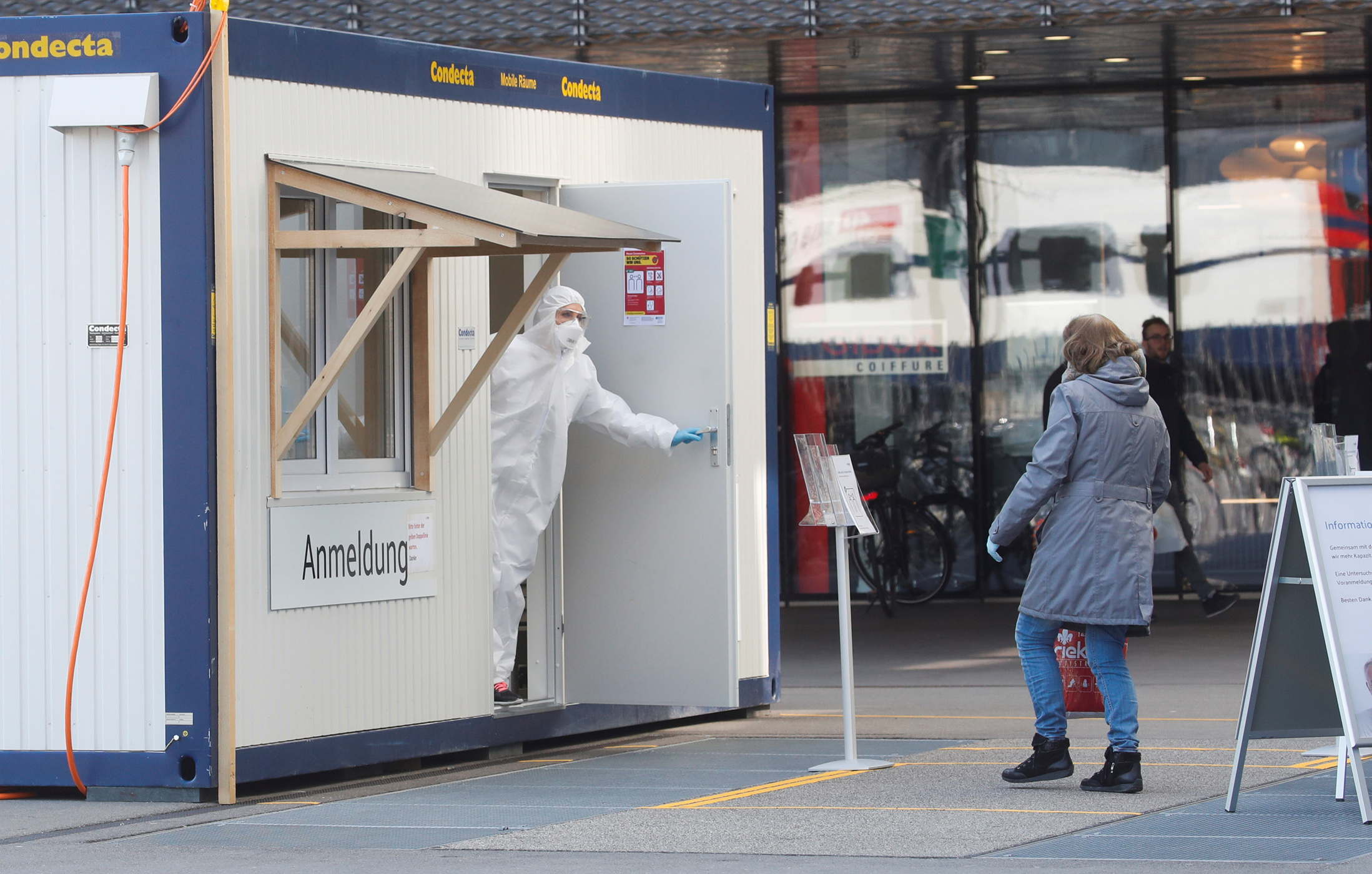 A health worker wearing a protection suit tells a woman that she can enter a container of Medbase medical center, used for tests on coronavirus disease (COVID-19), on a square in Winterthur, Switzerland March 24, 2020. REUTERS