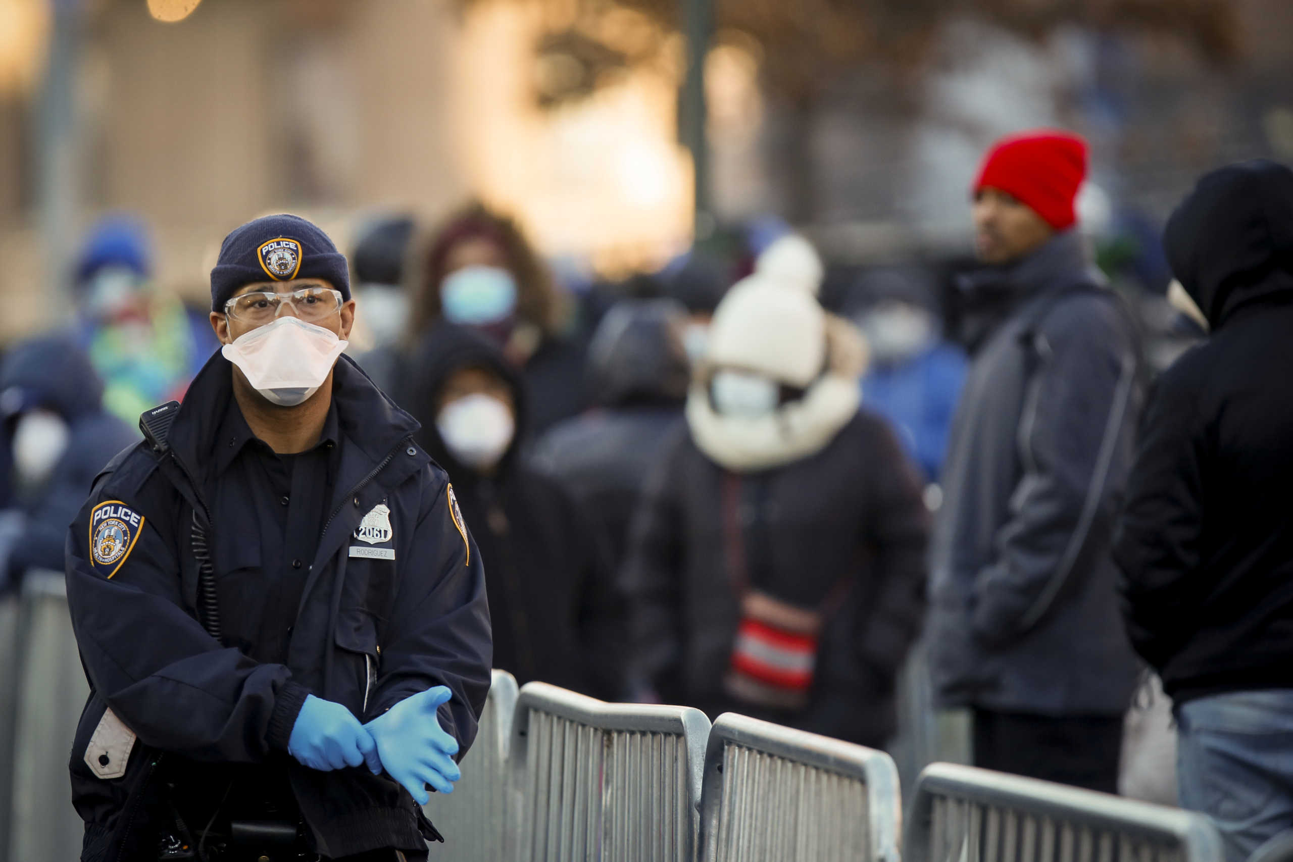 A New York City Police officer (NYPD) puts on gloves as people wait in line to be tested for coronavirus disease (COVID-19), outside Elmhurst Hospital Center in the Queens borough of New York City, U.S., March 26, 2020.  REUTERS