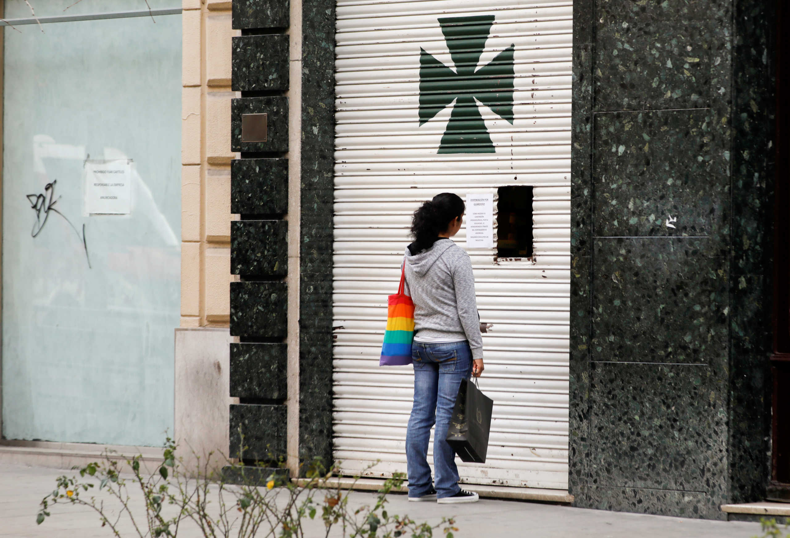 A woman waits as she buys through a window of a closed pharmacy due to the coronavirus outbreak, in downtown Granada, Spain March 13, 2020. REUTERS