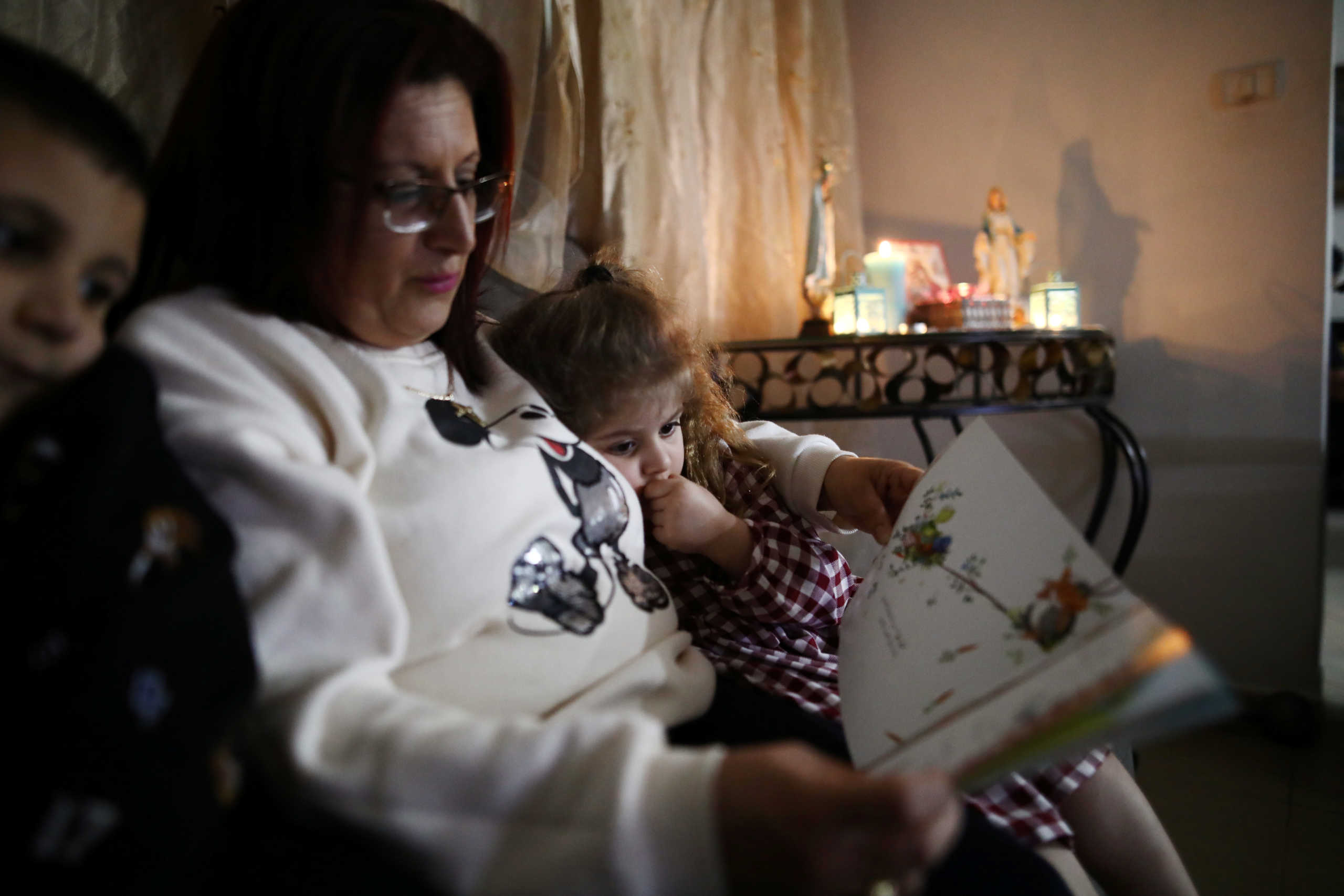 Palestinian woman Jizelle Sara, 42, reads a book to her children Elie, 6, and Silva, 5, while observing a partial lockdown to curb the spread of the coronavirus disease (COVID-19) at their home in Jerusalem March 25, 2020. Picture taken March 25, 2020. REUTERS