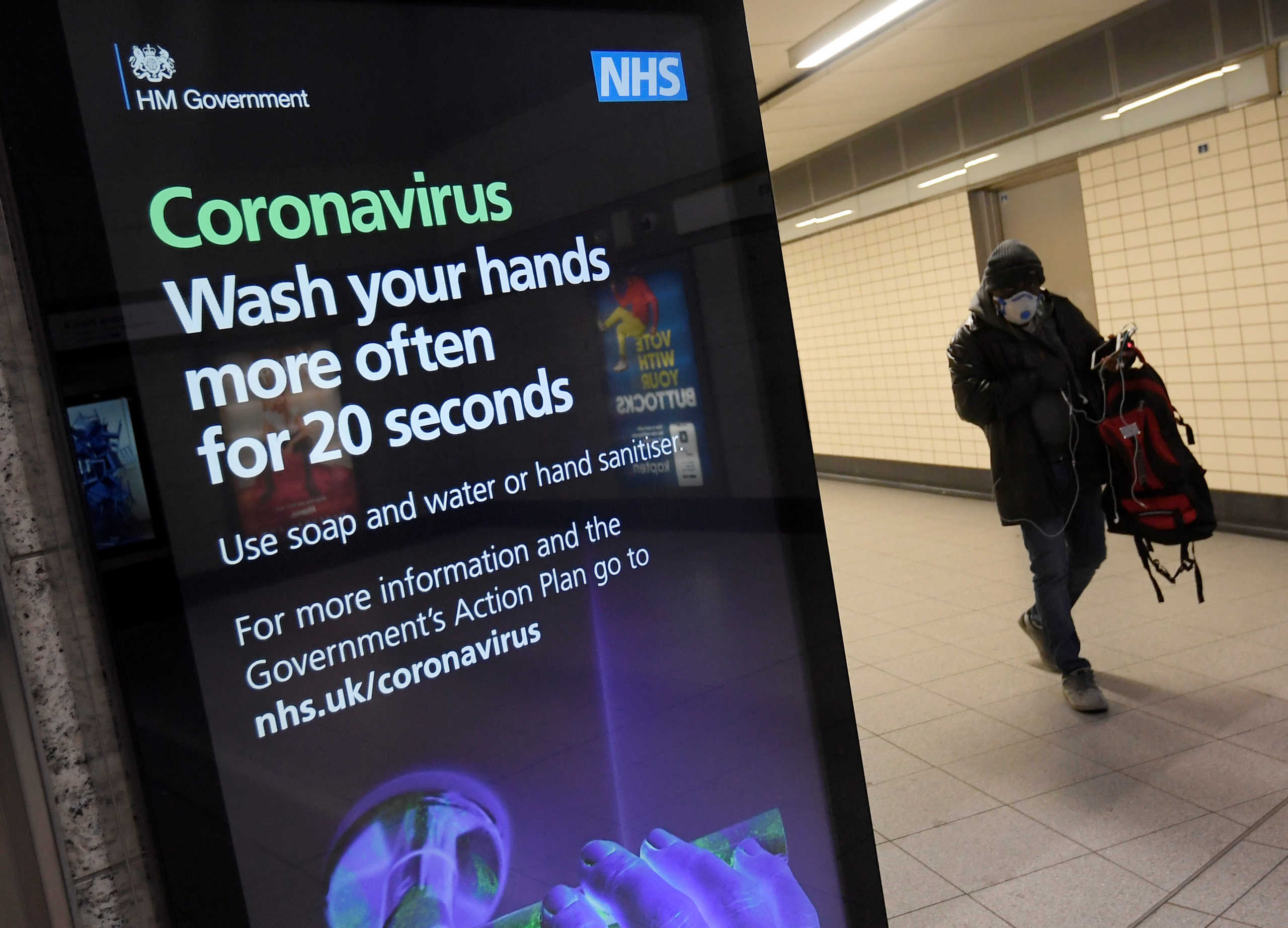 A man in a protective face mask walks past a British government public health campaign advertisement at Victoria underground station, as the number of coronavirus (COVID-19) cases grow around the world, London, Britain, March 15, 2020. REUTERS