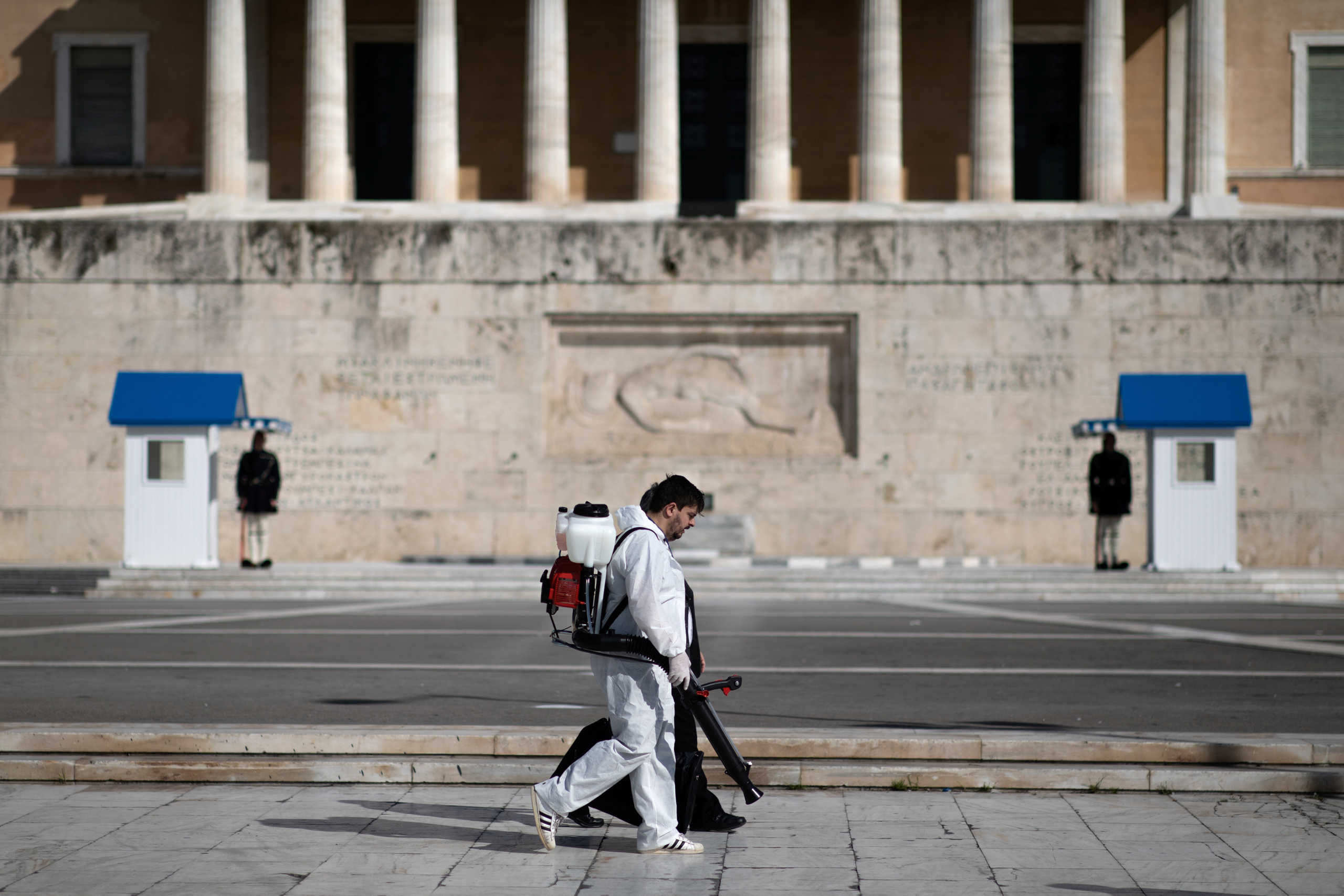 A worker in protective suit and carrying disinfection equipment walks past the parliament building in Athens, Greece, March 14, 2020. REUTERS