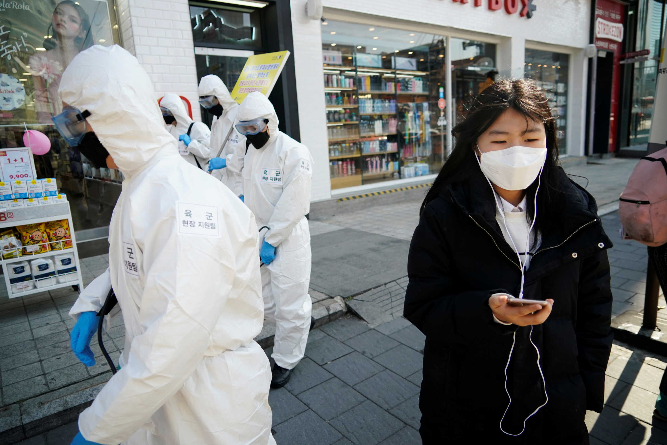 A woman wearing a mask as a preventive measure against the coronavirus walks past South Korean soldiers in protective gear sanitizing a street in Seoul, South Korea, March 5, 2020.   REUTERS