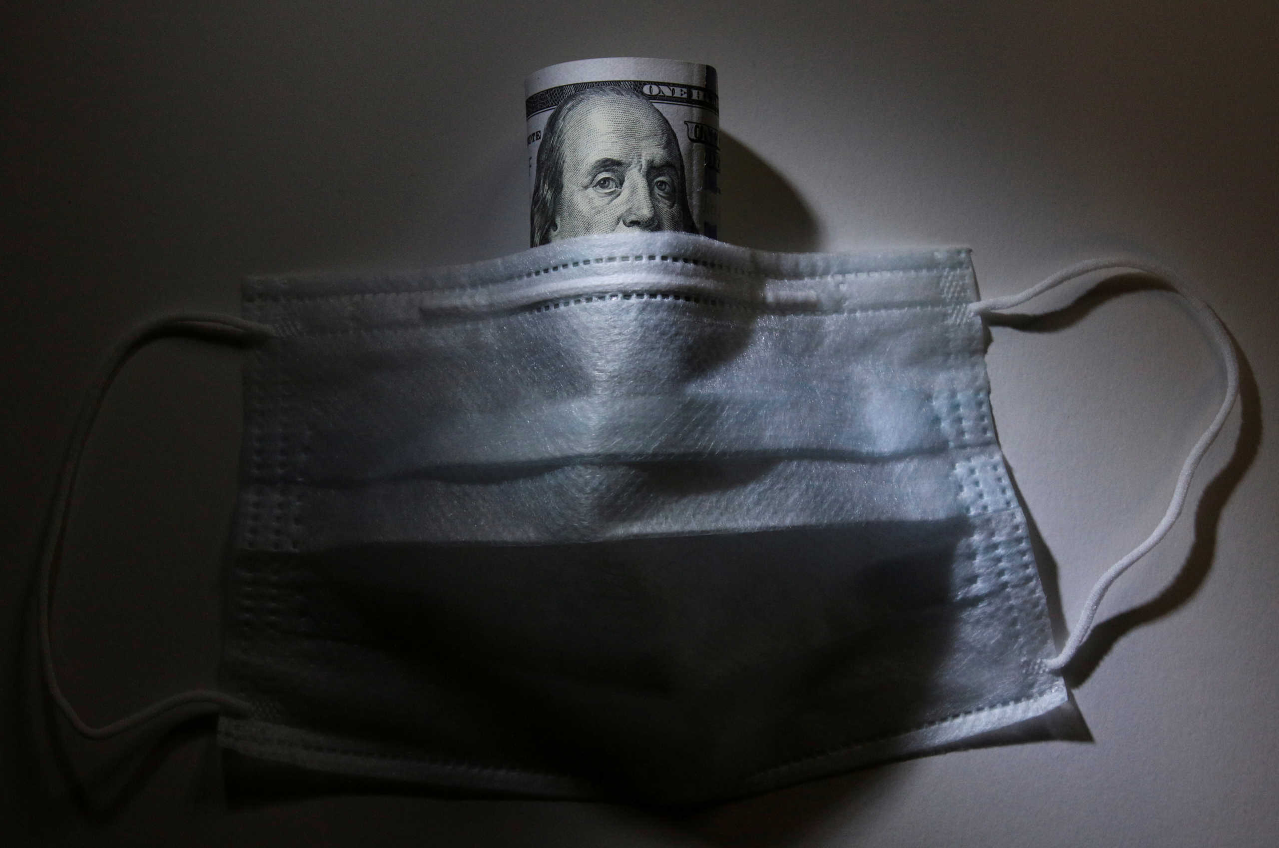FILE PHOTO: A U.S. dollar banknote is pictured behind a protective mask, which is widely used as a preventive measure against the coronavirus (COVID-19), in this illustration taken March 17, 2020. REUTERS