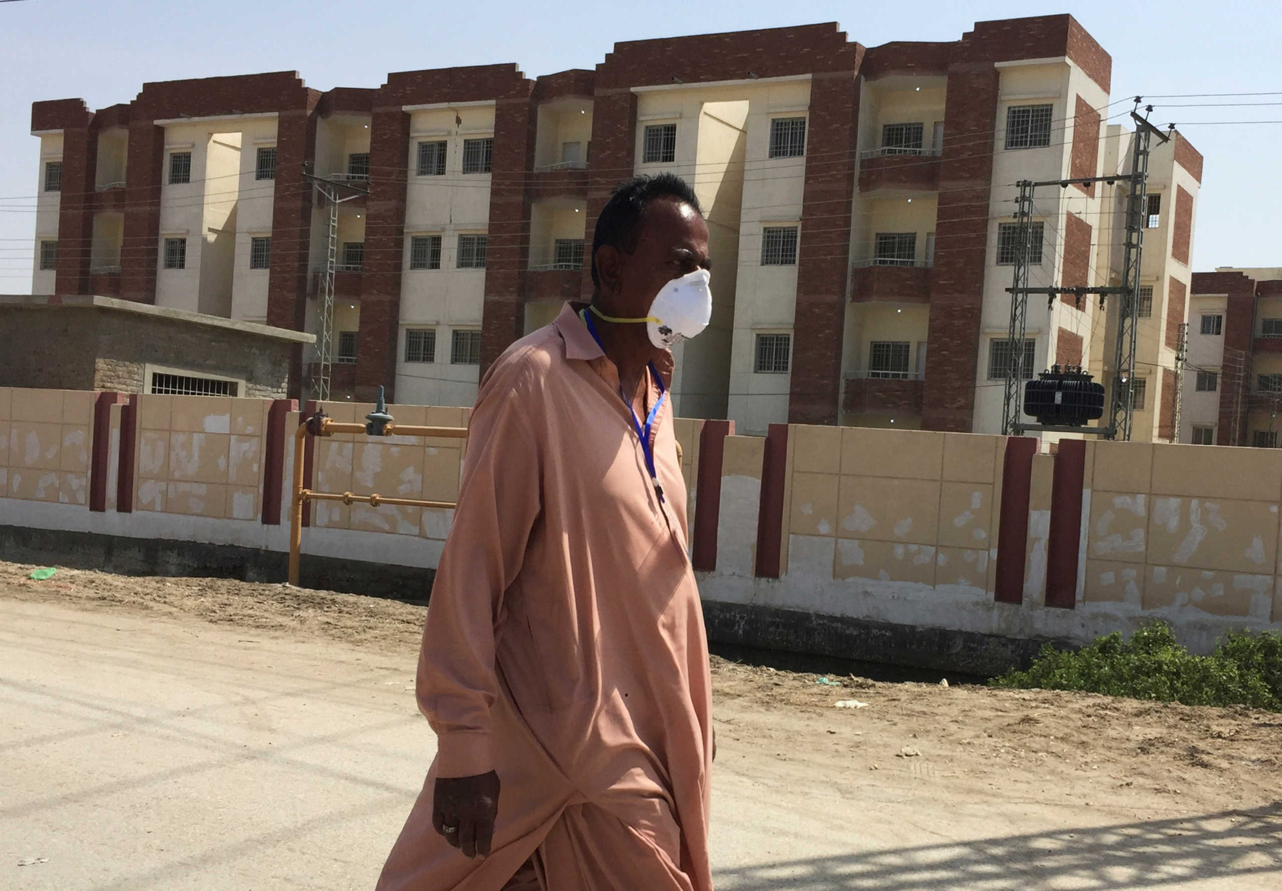A man wears a protective mask following an outbreak of the coronavirus disease (COVID-19), as he walks in front of buildings, declared by the government as quarantine for the suspected pilgrims, who crossed Taftan border post with Iran, in Sukkur, Pakistan March 18, 2020. REUTERS