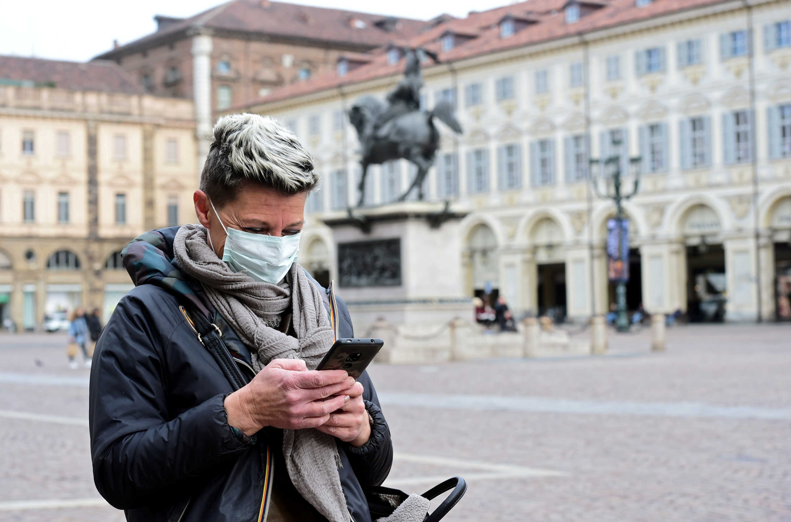 FILE PHOTO: A woman wearing a protective mask uses her mobile phone, as a coronavirus outbreak continues to grow in northern Italy, in Turin, Italy, February 27, 2020.  REUTERS