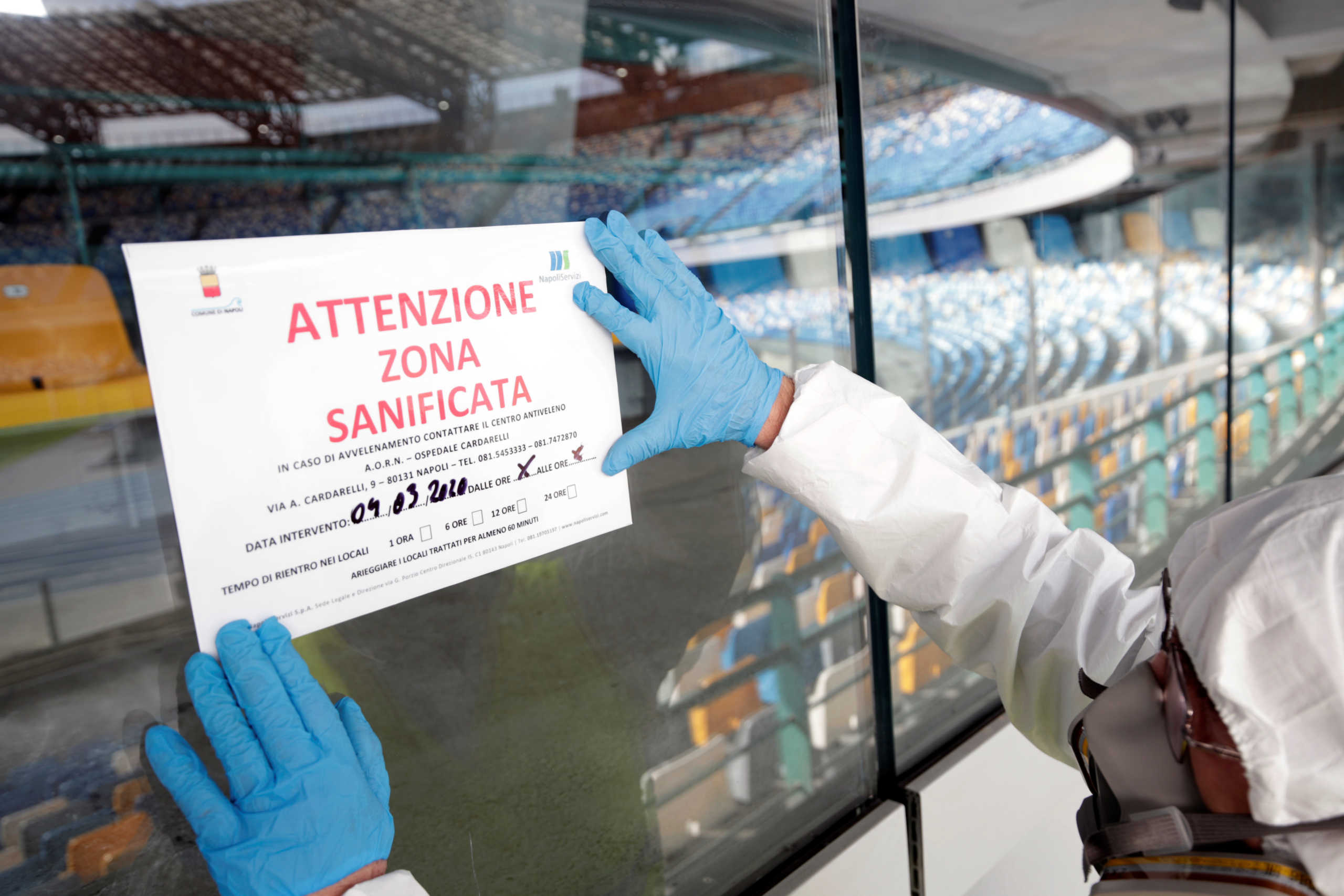 A cleaner wearing a protective suit adjusts a sign that reads "Attention: this zone has been sanitised" at the San Paolo stadium, ahead of the second leg of the Coppa Italia semi-final between Napoli and Inter Milan, which has since been postponed as part of measures to contain the coronavirus outbreak, in Naples, Italy, March 4, 2020. REUTERS