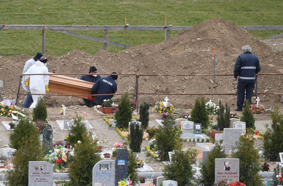 Workers place a coffin in the ground at a cemetery, as the spread of the coronavirus disease (COVID-19) continues, in Milan, Italy March 23, 2020. REUTERS