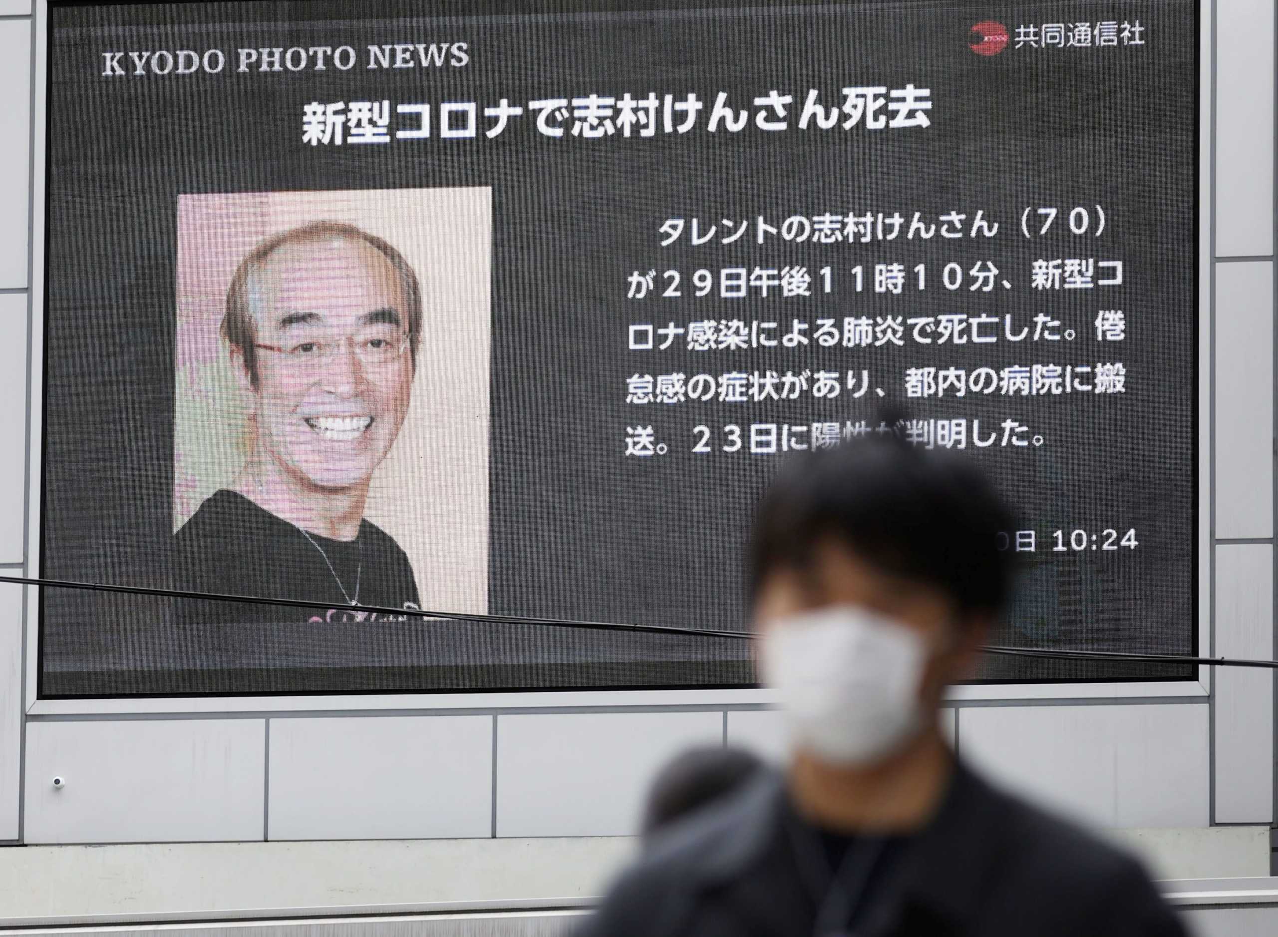 A man wearing a protective face mask, following an outbreak of the coronavirus disease (COVID-19), walks past in front of a huge screen reporting death of Japanese comedian Ken Shimura, who had been hospitalised after being infected with the new coronavirus, in Osaka, western Japan March 30, 2020, in this photo taken by Kyodo. Mandatory credit Kyodo