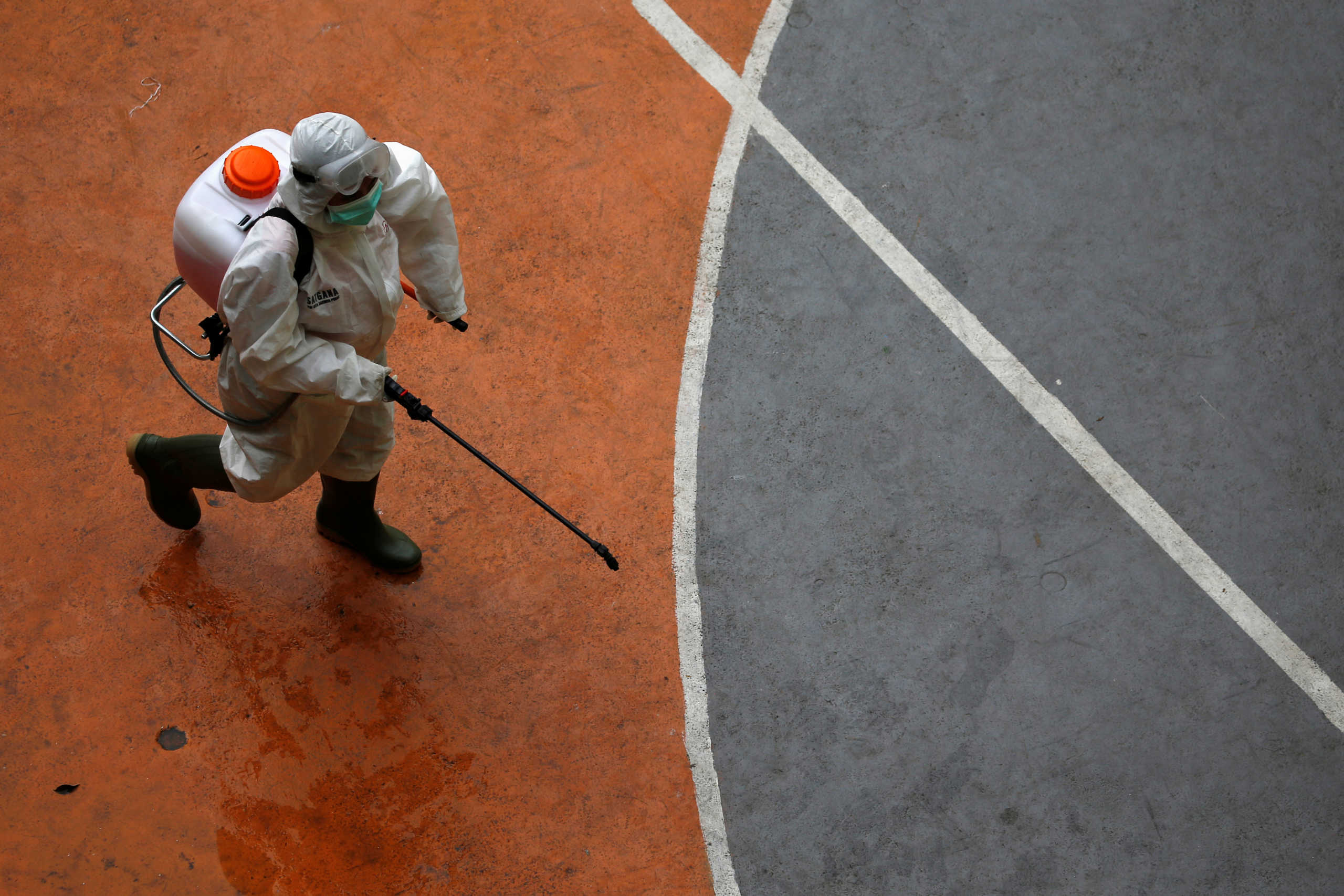 A volunteer from Indonesia's Red Cross, wearing a protective suit, walks while carrying a disinfectant sprayer at a school closed amid the spread of coronavirus (COVID-19) in Jakarta, Indonesia, March 16, 2020. REUTERS