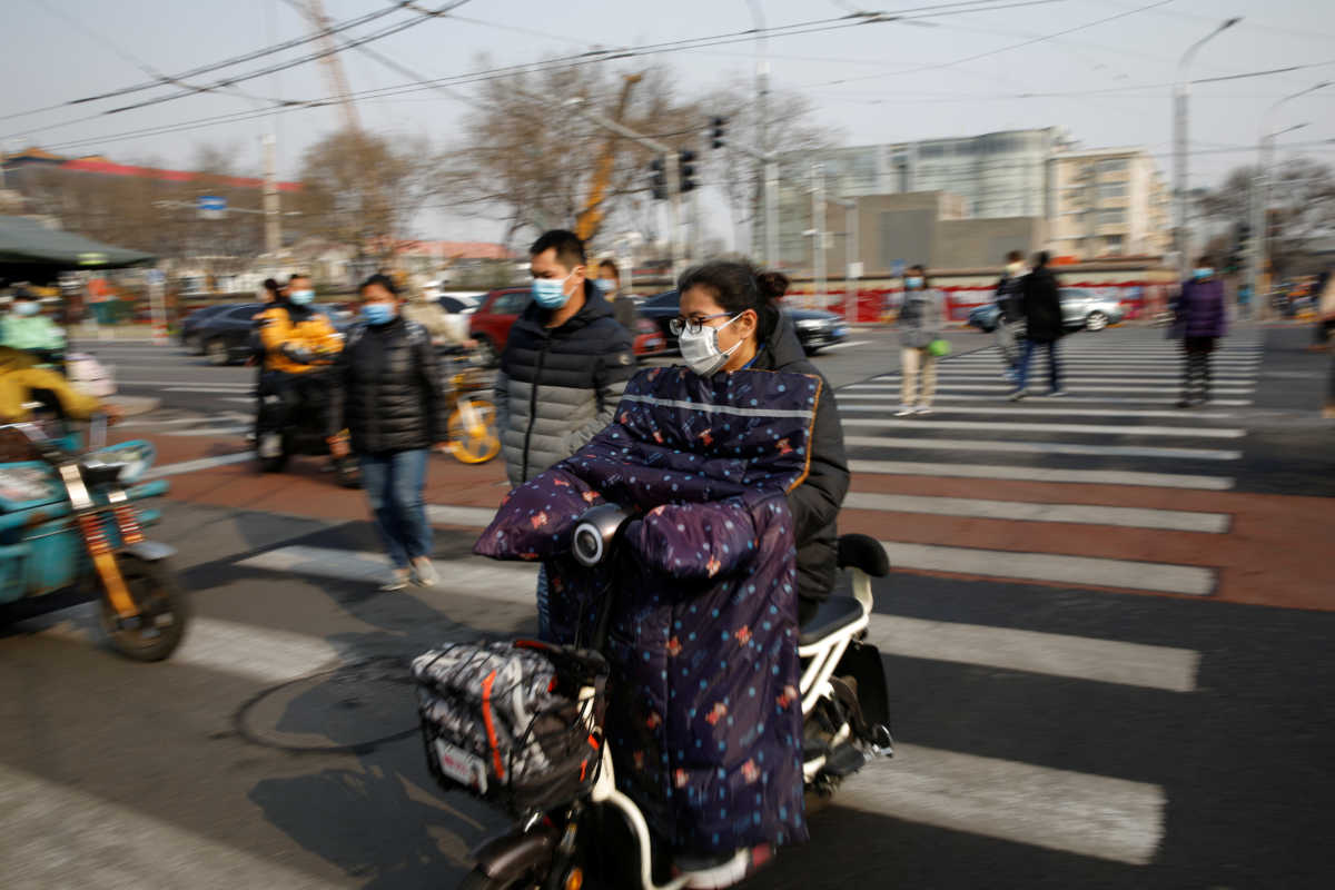 People wearing face masks ride their scooters and  walk on a street following an outbreak of the coronavirus disease (COVID-19), in Beijing, China March 30, 2020. REUTERS