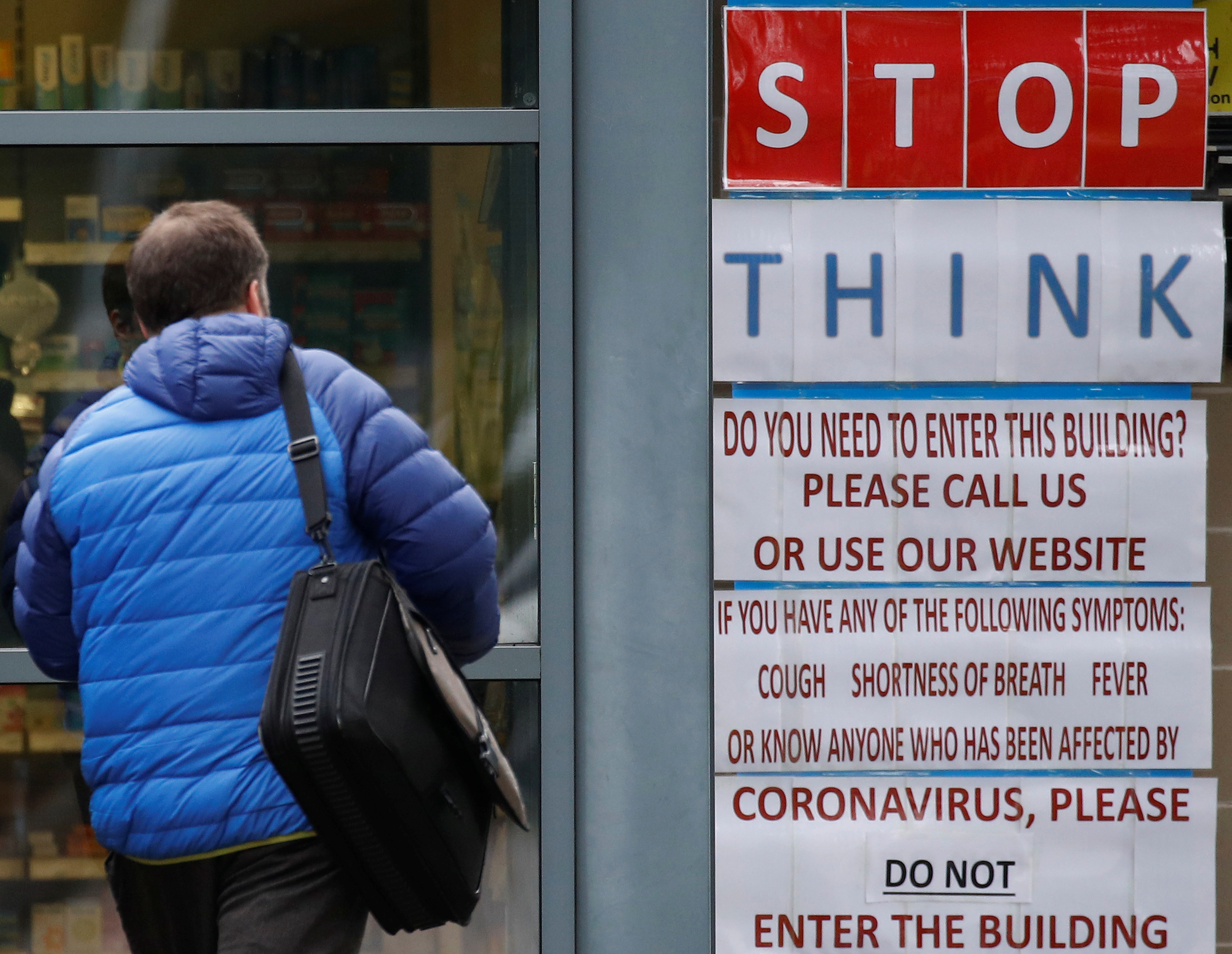 A man walks towards a coronavirus warning sign outside a medical centre in Manchester, Britain March 18, 2020. REUTERS