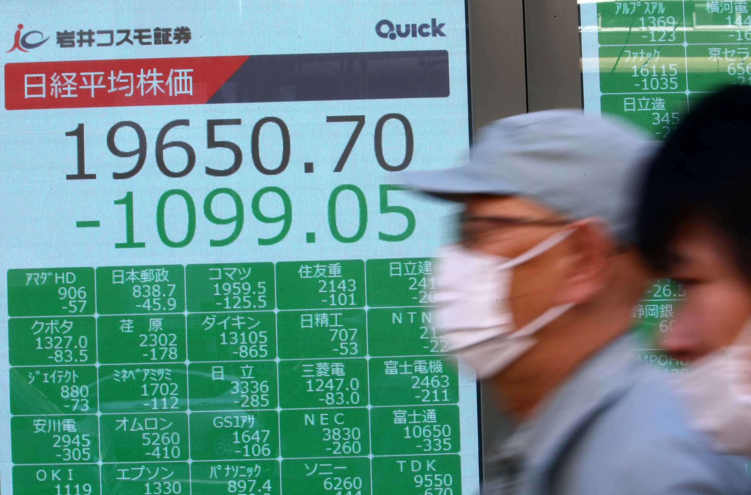 People wearing protective face masks walk past an electronic display showing Asian markets indices outside a brokerage in Tokyo, Japan, following an outbreak of the coronavirus disease (COVID-19),   March 9, 2020. REUTERS