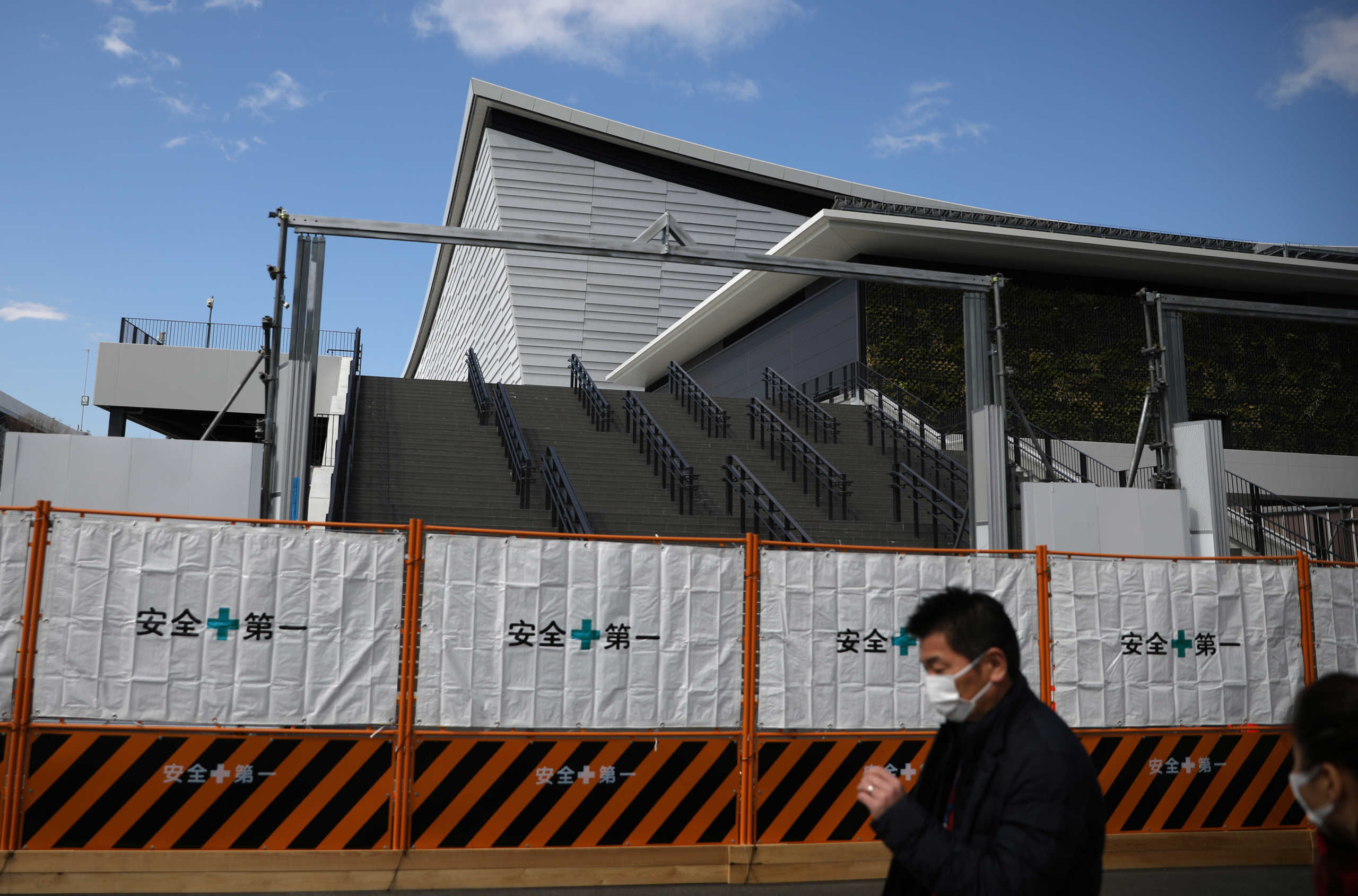People wearing protective face masks, following an outbreak of the coronavirus disease (COVID-19), walk past Ariake Arena, a venue for the upcoming Tokyo 2020 Olympic Games volleyball competitions, in Tokyo, Japan, March 12, 2020. REUTERS