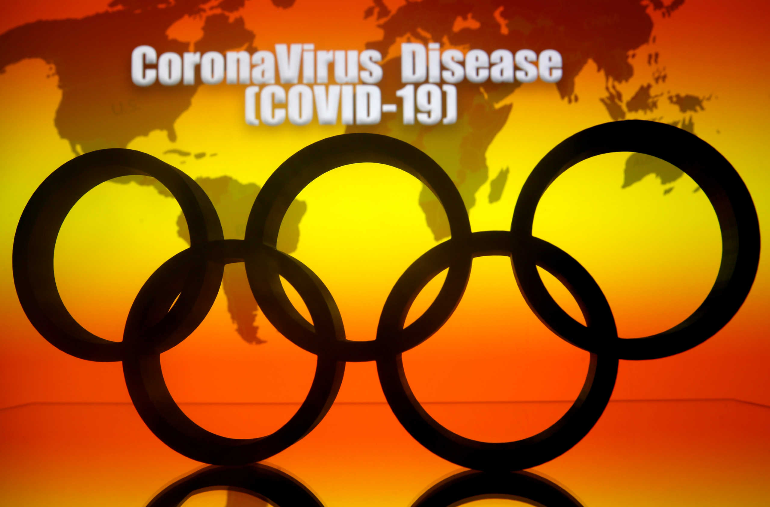 A 3D printed Olympics logo is seen in front of displayed world map and  "Coronavirus Disease (COVID-19)" words in this illustration taken March 23, 2020 REUTERS