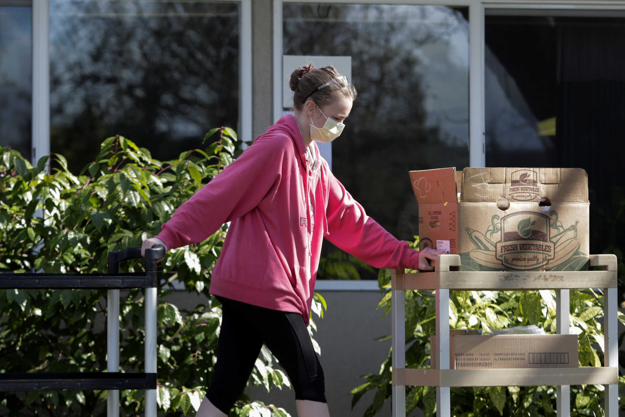 A woman in a mask moves boxes of goods that were dropped off at Shuksan Healthcare Center during an outbreak of coronavirus disease (COVID-19) among residents and staff, in Bellingham, Washington, U.S. March 23, 2020.  REUTERS