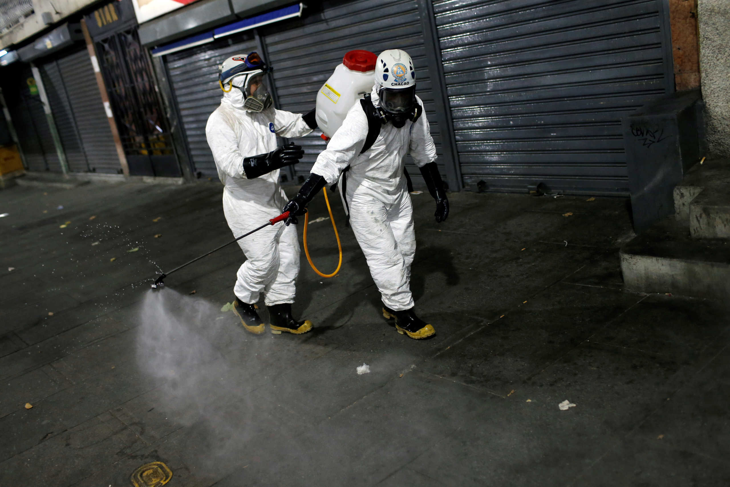 Workers wearing protective suits spray disinfectant solution in the street during the national quarantine in response to the spread of coronavirus disease (COVID-19) in Caracas, Venezuela March 22, 2020. REUTERS