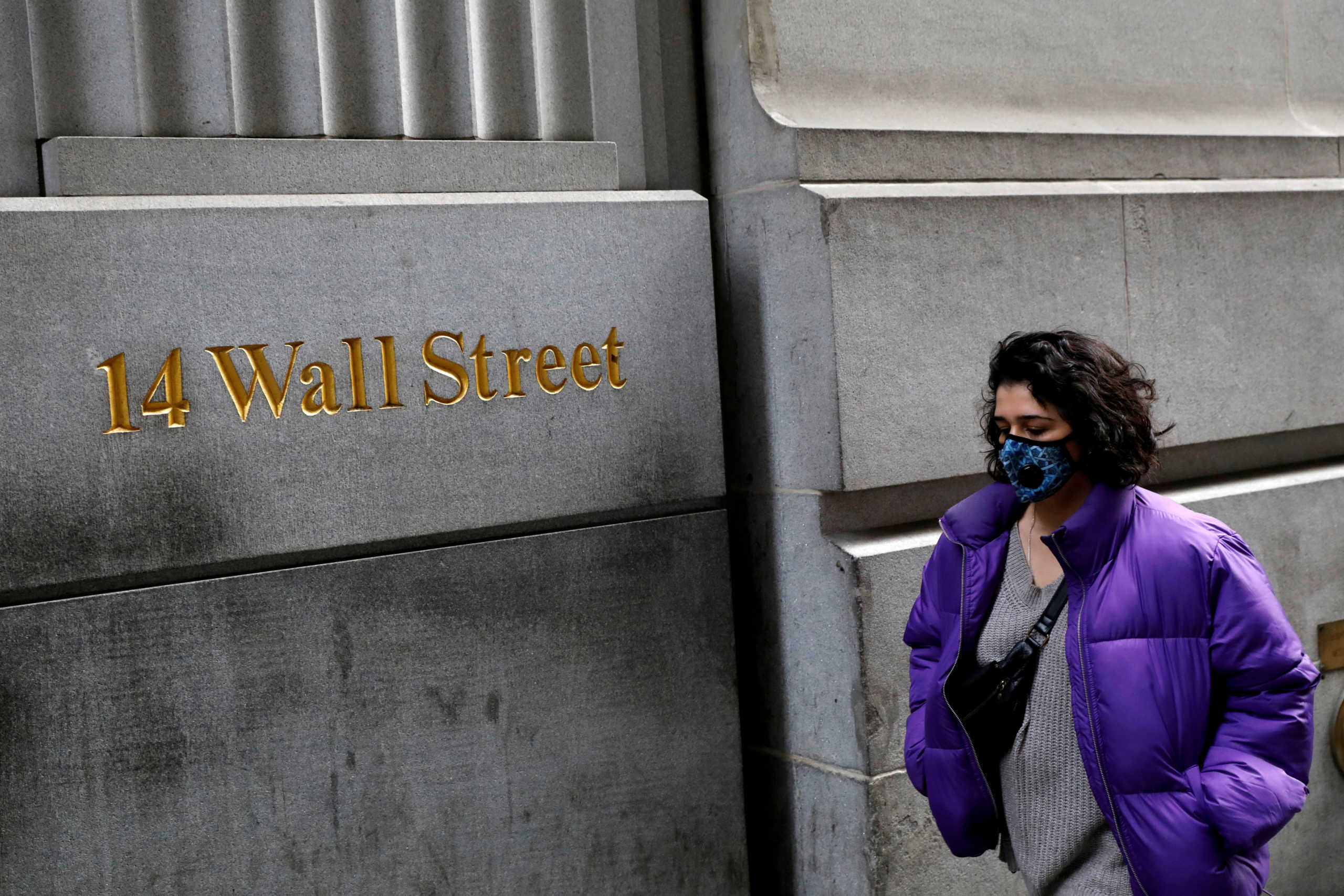 FILE PHOTO: A person wearing a face mask walks along Wall Street after further cases of coronavirus were confirmed in New York City, New York, U.S., March 6, 2020. REUTERS