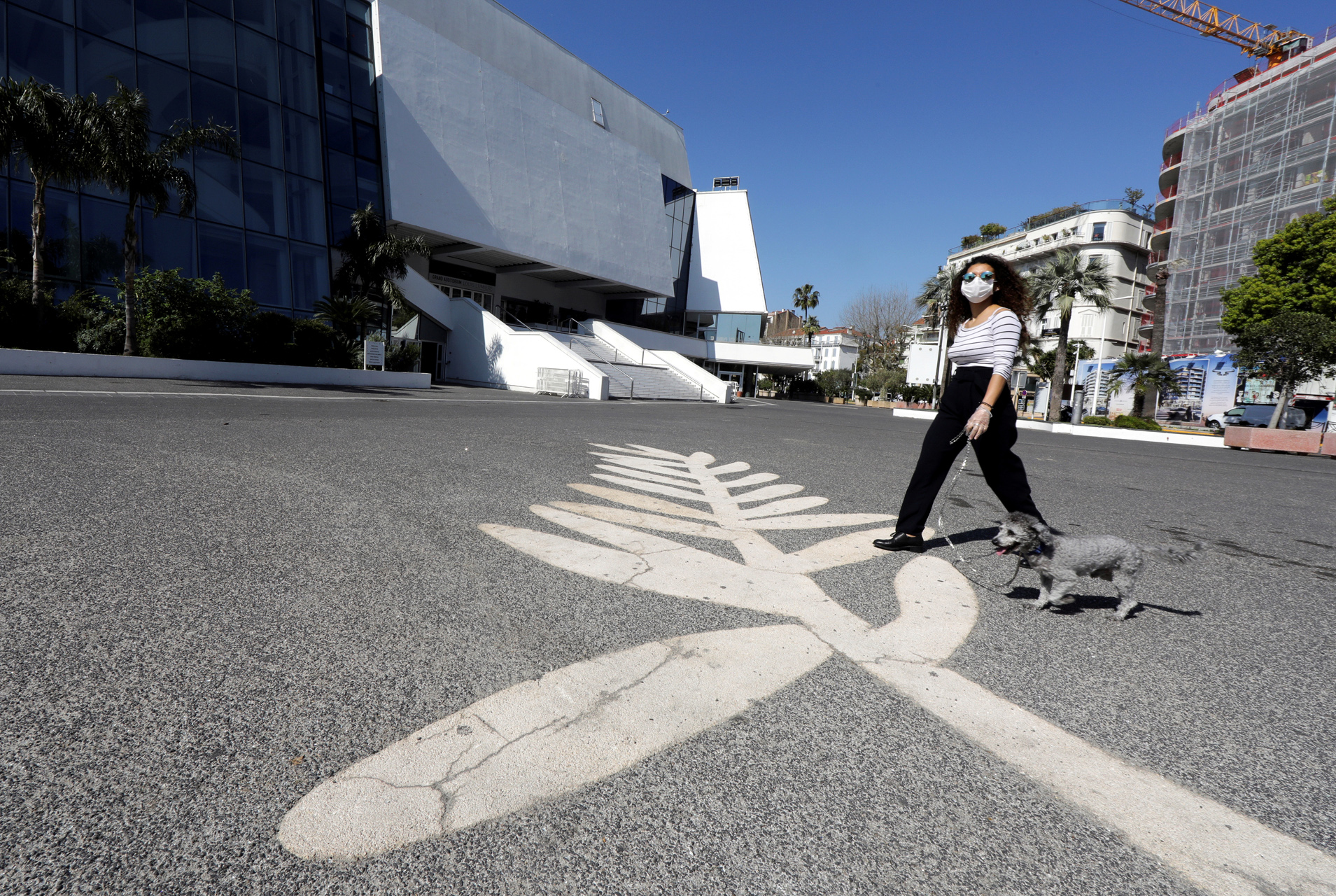 FILE PHOTO: A woman wearing a protective face mask walks her dog past a Palme d'Or symbol on the pavement near the Festival palace on the Croisette in Cannes where the Cannes Film Festival and the Cannes Lions take place, as a lockdown is imposed to slow the rate of the coronavirus disease (COVID-19), in France, March 18, 2020. REUTERS