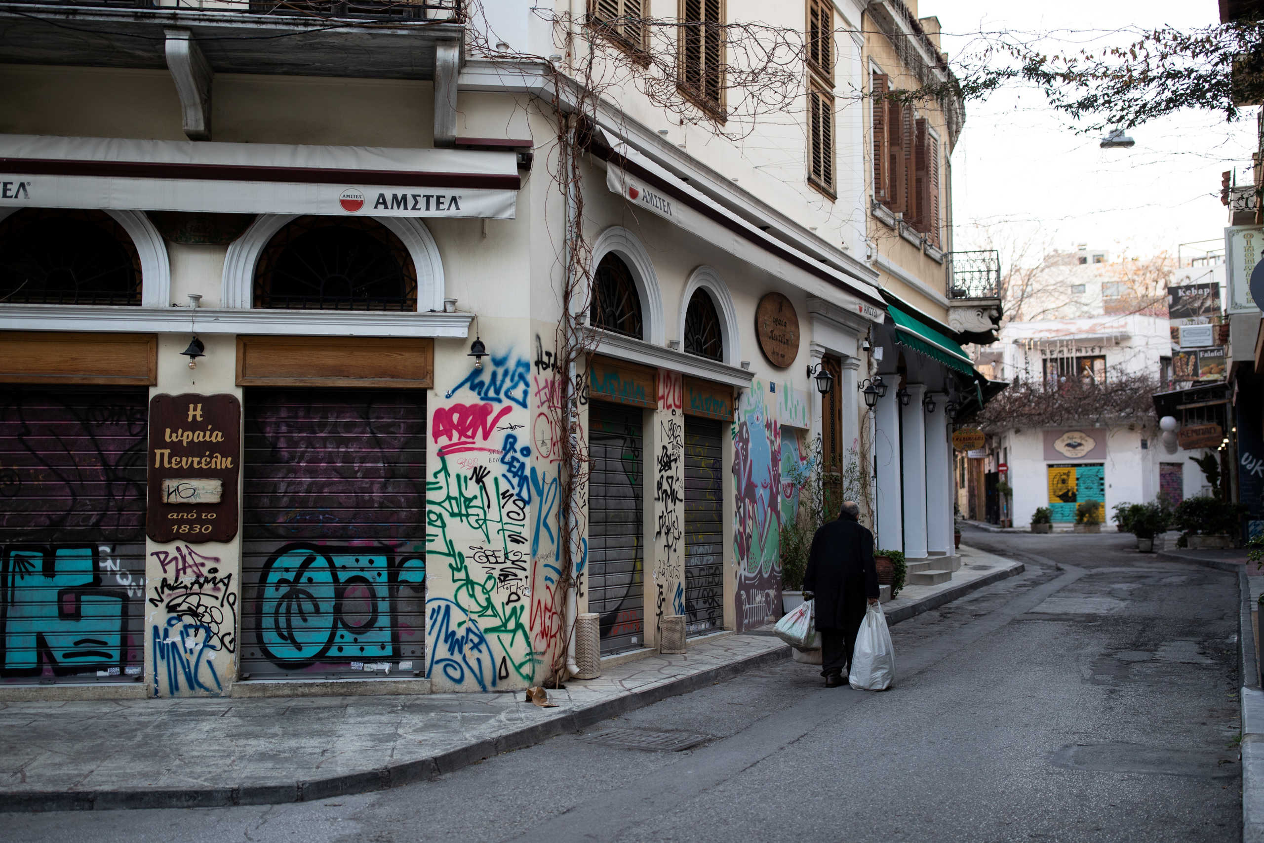 A man carries bags as he makes his way next to closed restaurants, during a nationwide lockdown to contain the spread of the coronavirus disease (COVID-19), in Athens, Greece, March 30, 2020. REUTERS