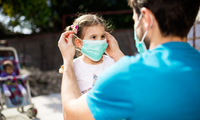 Single father applying pollution mask to his daughter. They are outside.
