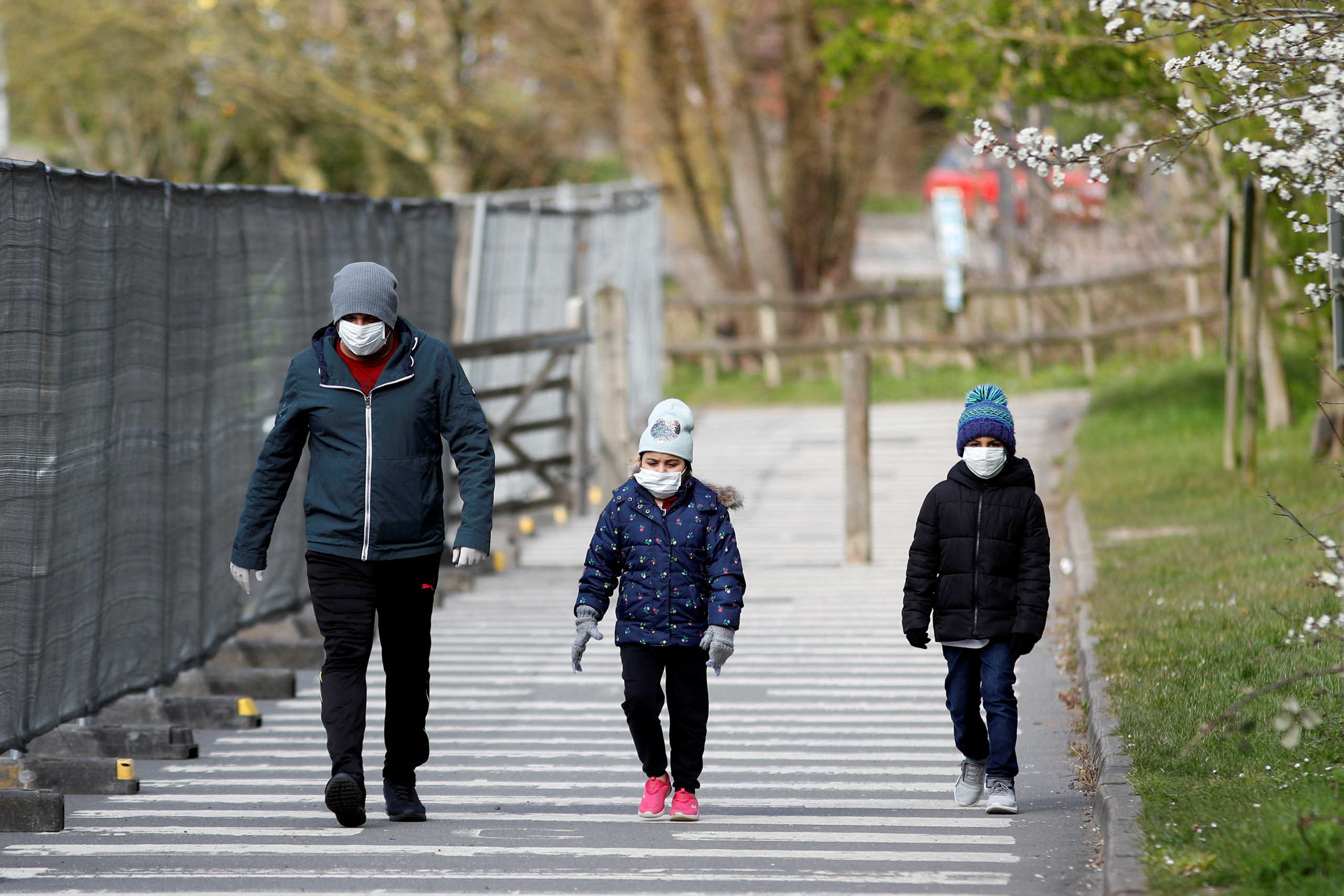 A man and children wearing protective face masks walk near a Chessington World of Adventures car park, which has been turned into a testing facility as the spread of the coronavirus disease (COVID-19) continues, Chessington, Britain, March 28, 2020. REUTERS