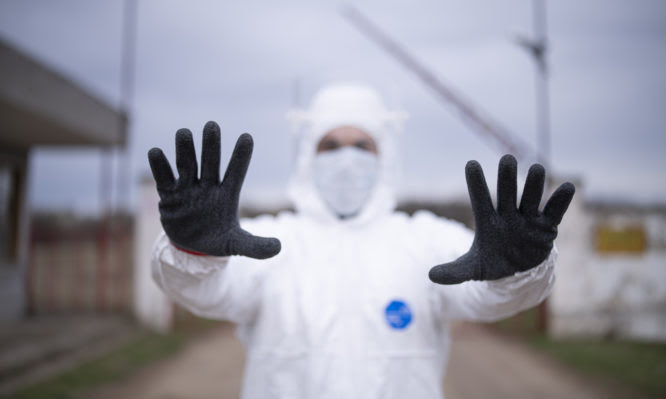 Worker with protective suit sign STOP with hand on border traffic, closed border, COVID-19 pandemic.