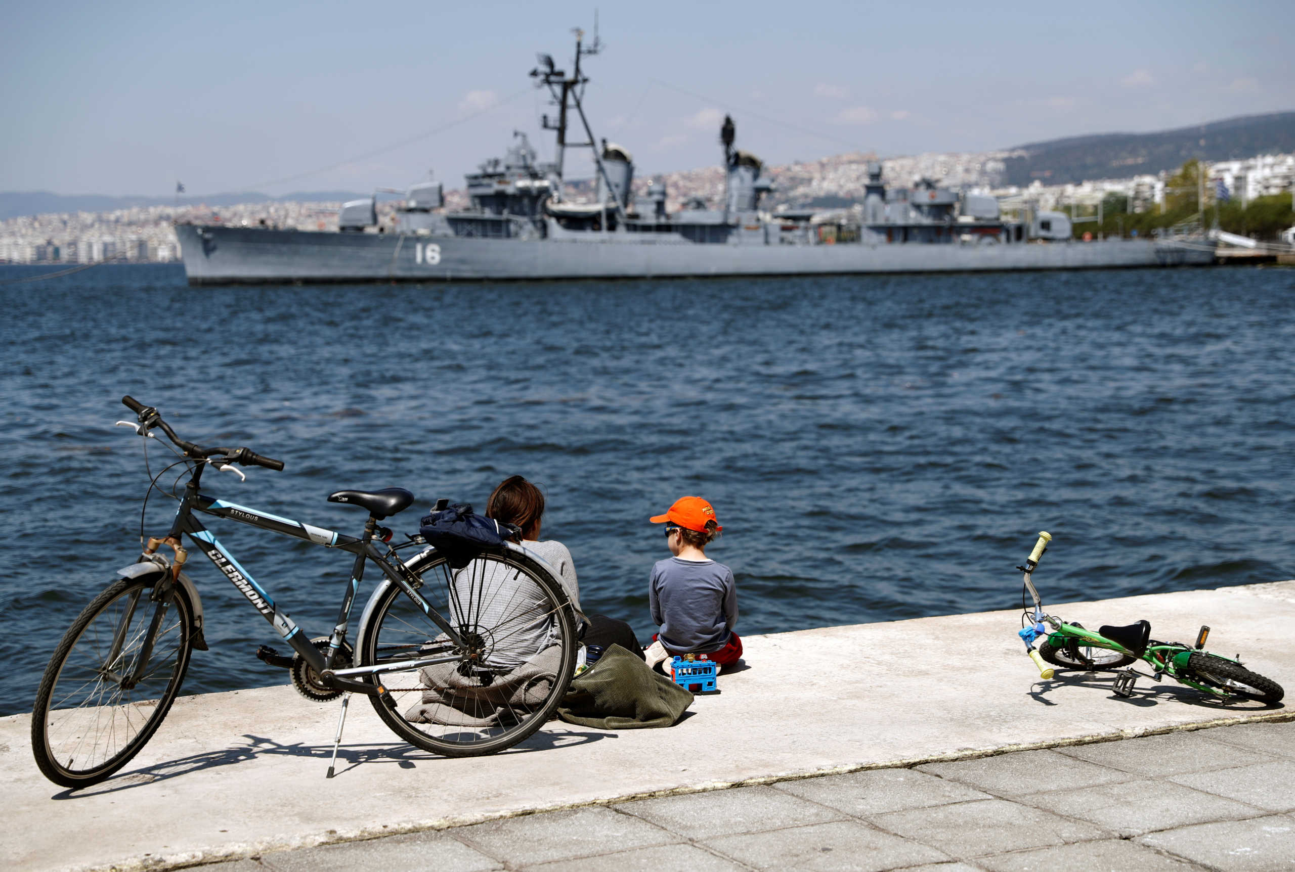 A woman and a boy pause at the seaside promenade as the coronavirus disease (COVID-19) outbreak continues, in Thessaloniki, Greece, April 24, 2020. Hellenic Navy destroyer Velos (D 16), now a floating naval museum, is seen in the background. REUTERS