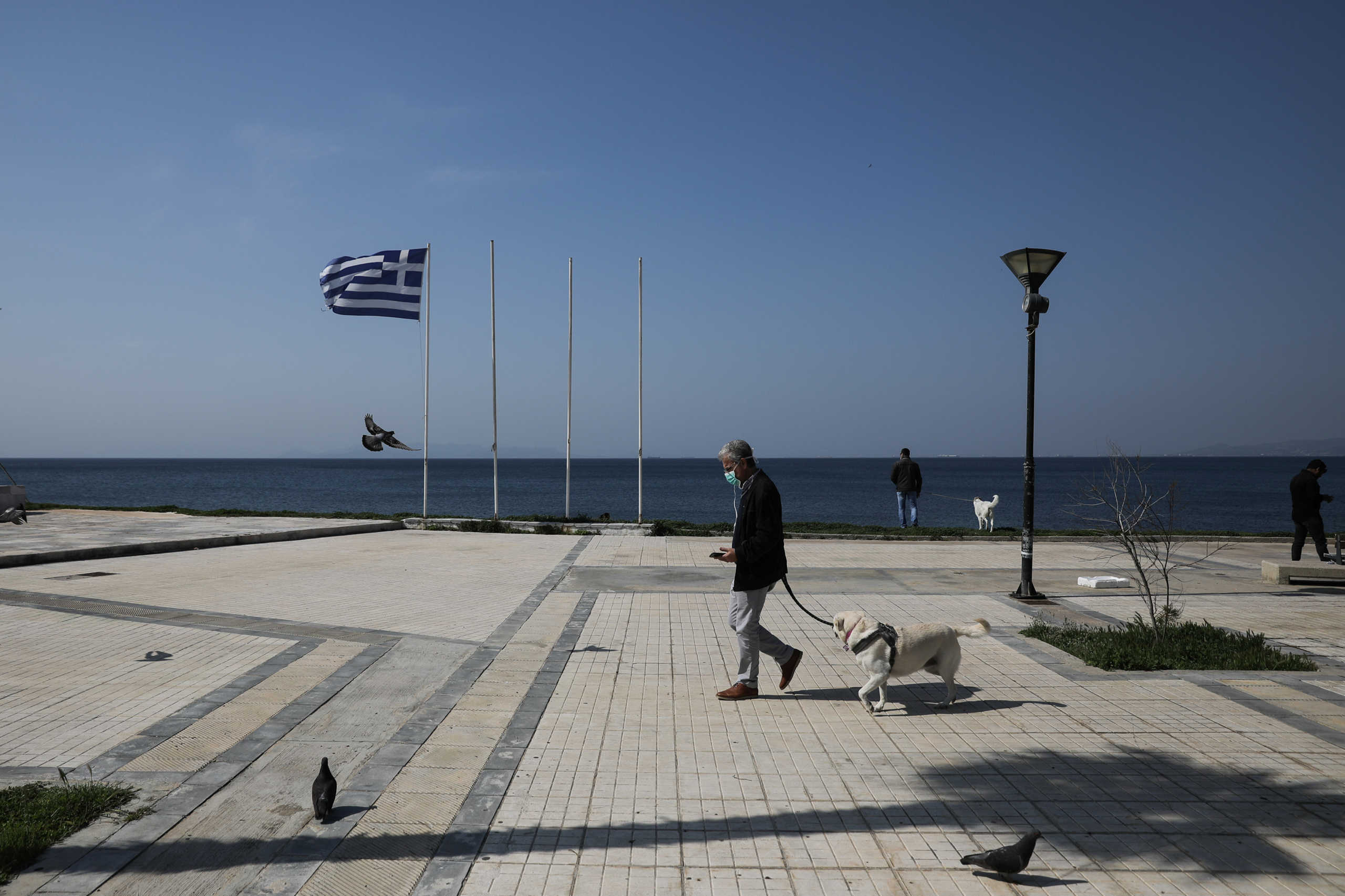 A man wearing a protective face mask walks his dog on a seaside promenade, following the outbreak of coronavirus disease (COVID-19), in Athens, Greece, March 31, 2020. REUTERS