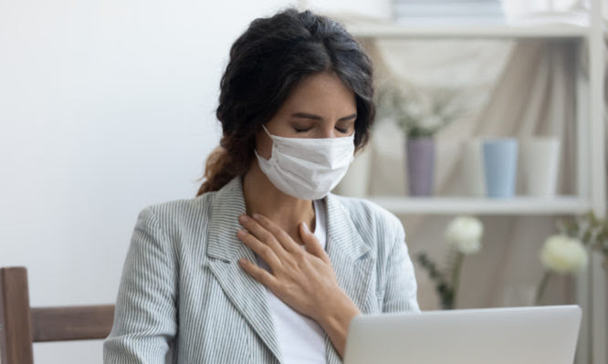 Business woman in mask sitting at desk feels unhealthy put hand where is lungs, suffering from repeated coughing and breath difficulties. Risk coronavirus 2019-ncov contamination at workplace concept