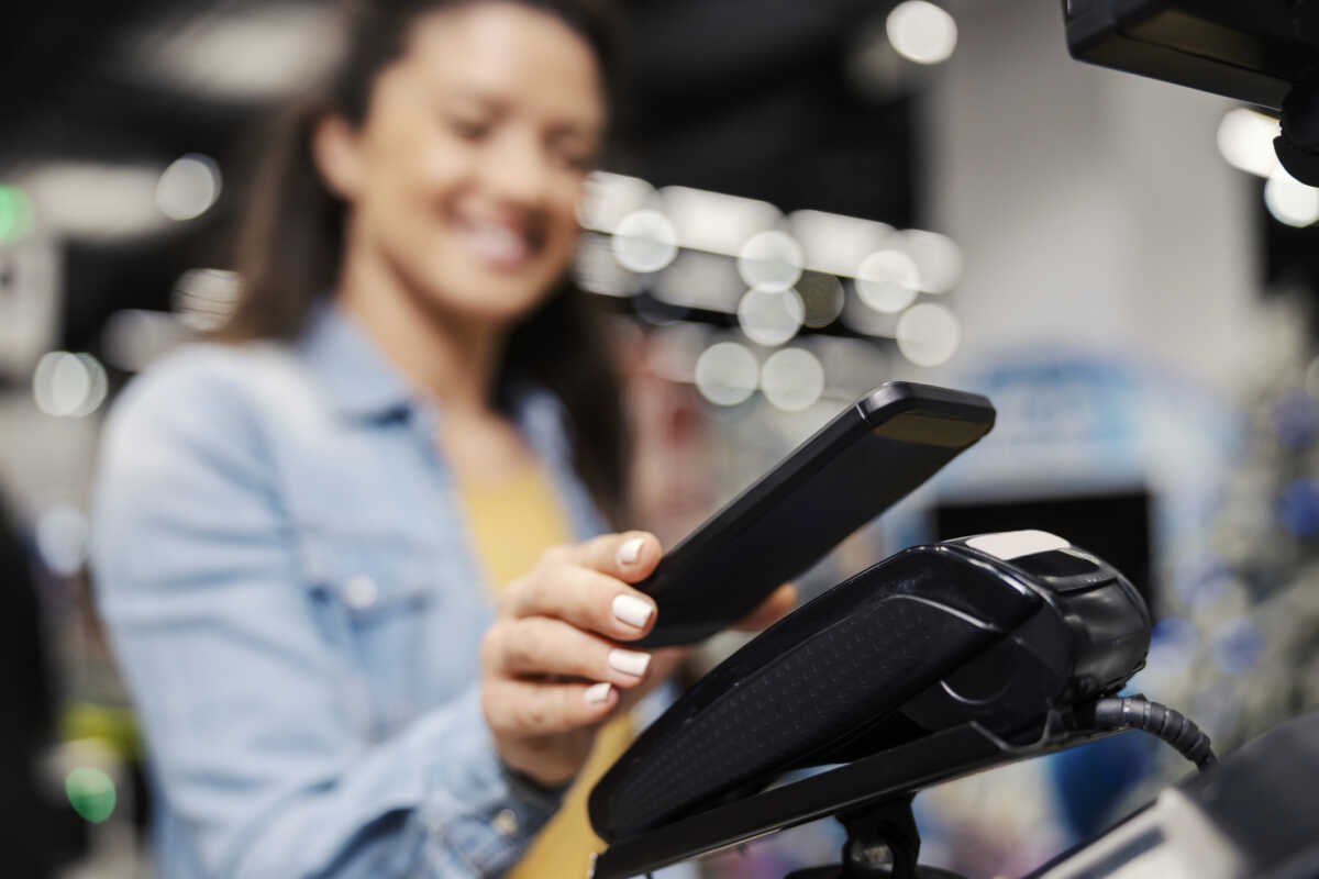 Close up of a female's hand paying bill on pos terminal with phone app at supermarket.