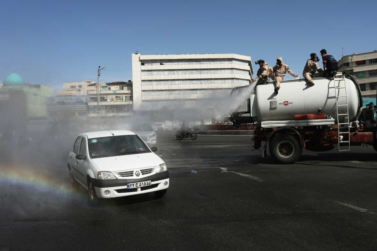 A car passes on the street as volunteers from Basij forces wearing protective suits and face masks spray disinfectant, amid the coronavirus disease (COVID-19) fears, in Enghelab square in Tehran, Iran April 3, 2020. WANA (West Asia News Agency)