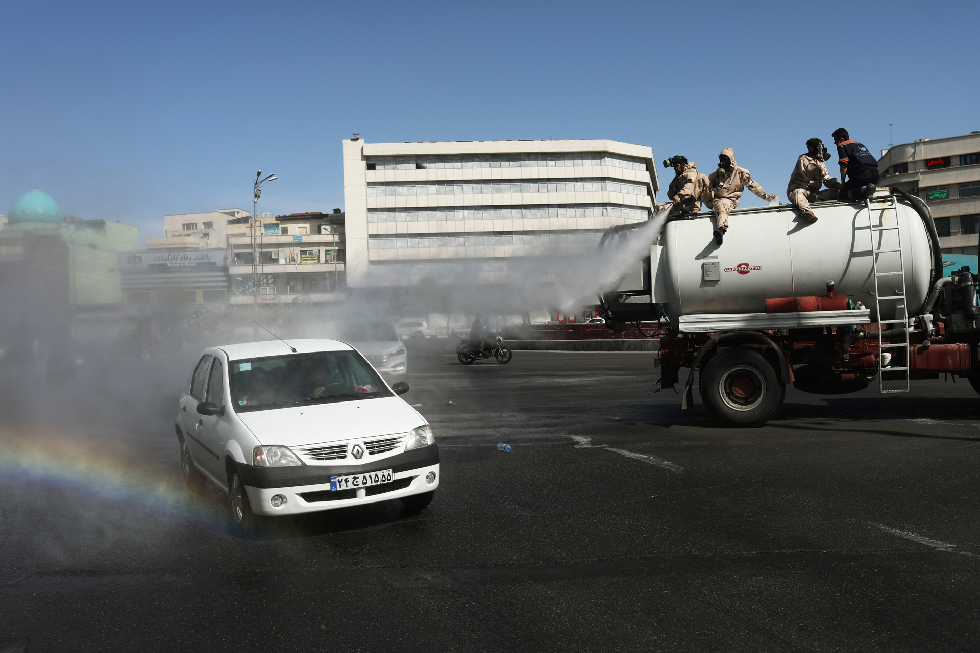 A car passes on the street as volunteers from Basij forces wearing protective suits and face masks spray disinfectant, amid the coronavirus disease (COVID-19) fears, in Enghelab square in Tehran, Iran April 3, 2020. WANA (West Asia News Agency)