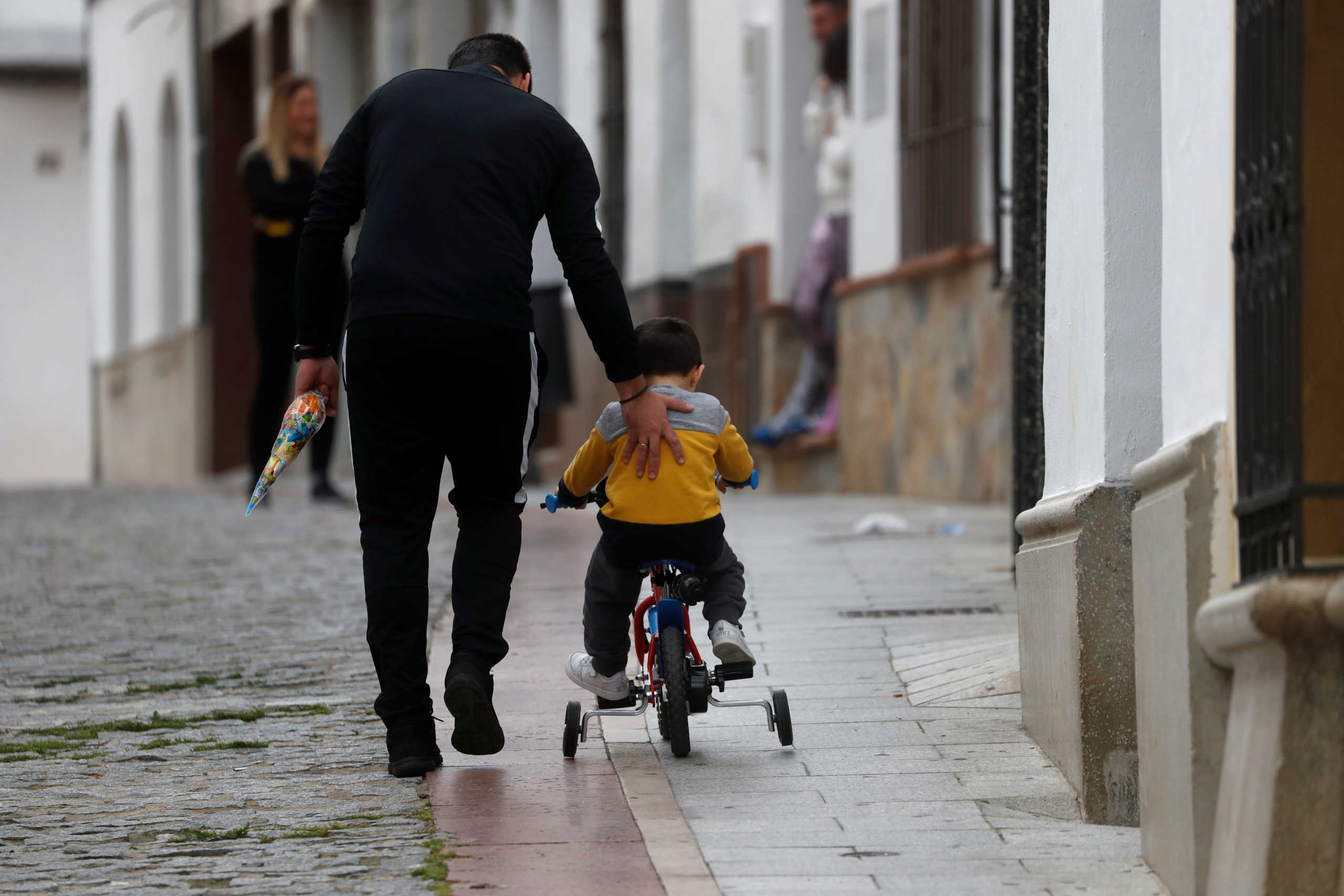 A man pushes his son riding a bicycle in a street, after restrictions were partially lifted for children for the first time in six weeks, during the coronavirus disease (COVID-19) outbreak in Ronda, Spain, April 26, 2020. REUTERS