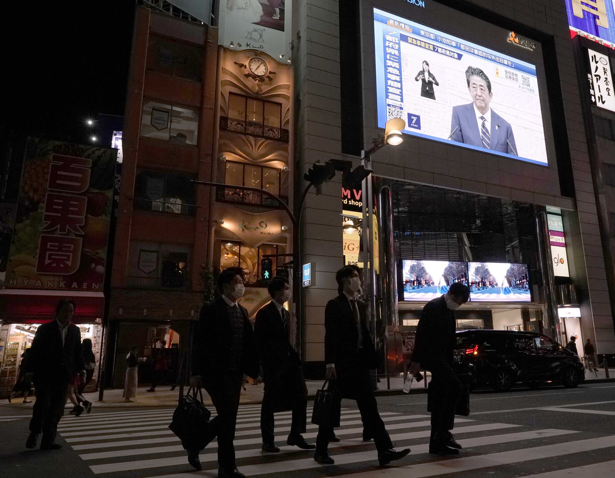 Pedestrians, wearing protective masks, walk past a large screen on a building showing Japan's Prime Minister Shinzo Abe declaring state of emergency, following the coronavirus disease (COVID-19) outbreak, in Tokyo, Japan April 7, 2020.  REUTERS