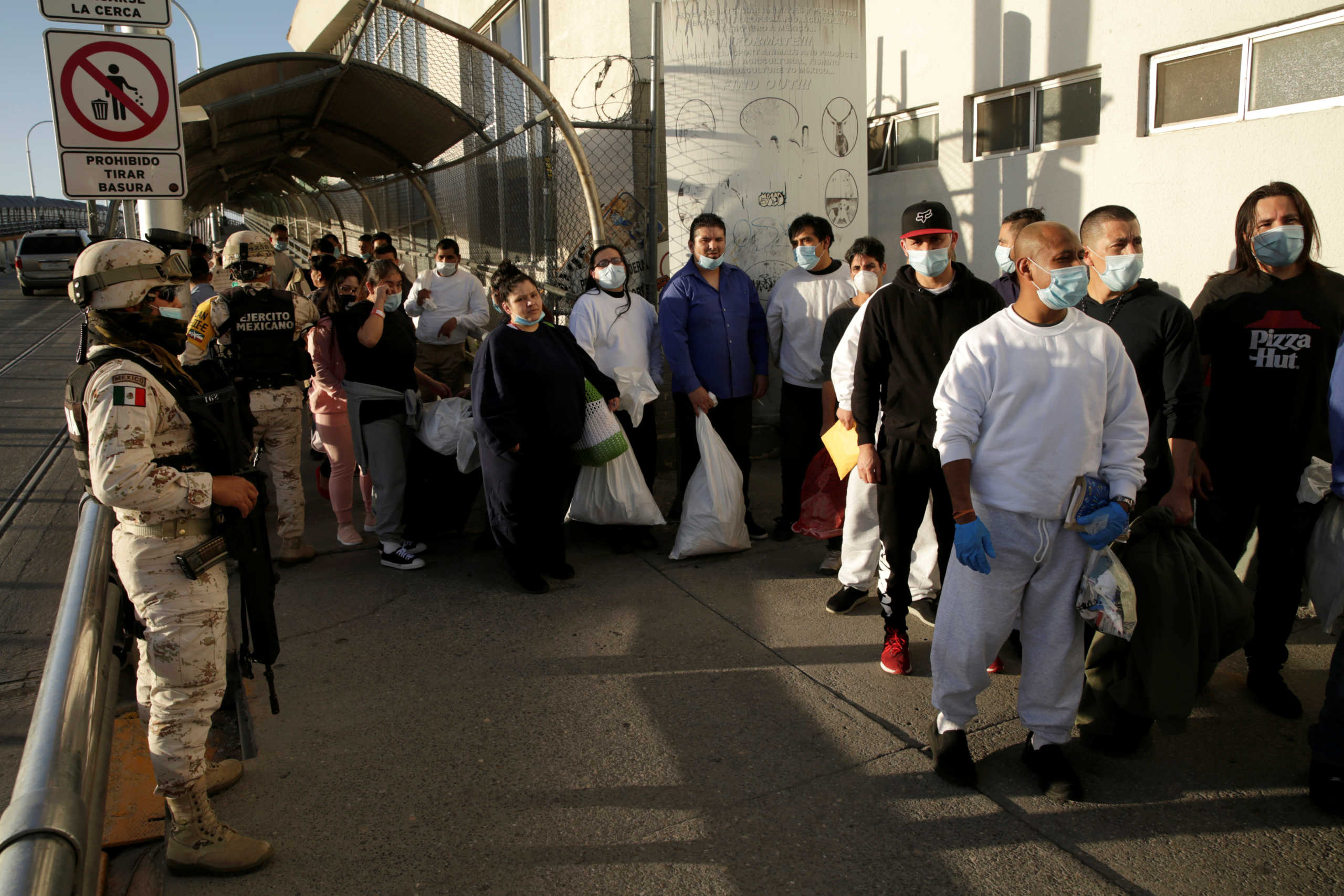Mexican immigrants wait beside members of the Mexican army outside of a National Institute of Migration (INM) building after being deported from the United States and crossing the Paso del Norte border bridge amid the spread of the coronavirus disease (COVID-19), in Ciudad Juarez, Mexico April 21, 2020. REUTERS