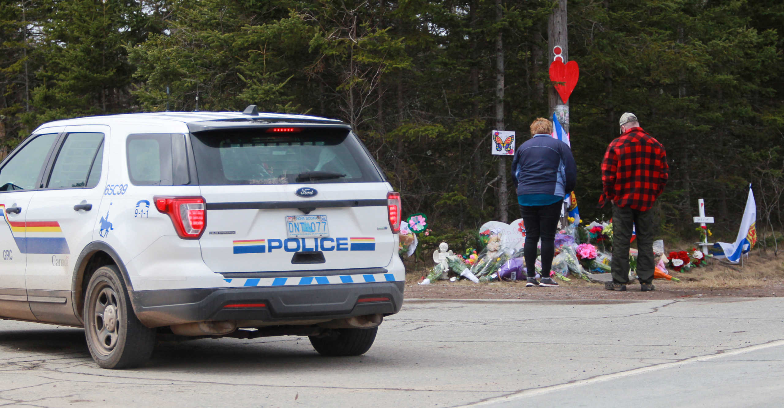 Mourners pay their respects in front of the makeshift memorial, made in the memory for the victims of Sunday’s mass shooting as a Royal Canadian Police Vehicle passes nearby in Portapique, Nova Scotia, Canada April 23, 2020. REUTERS