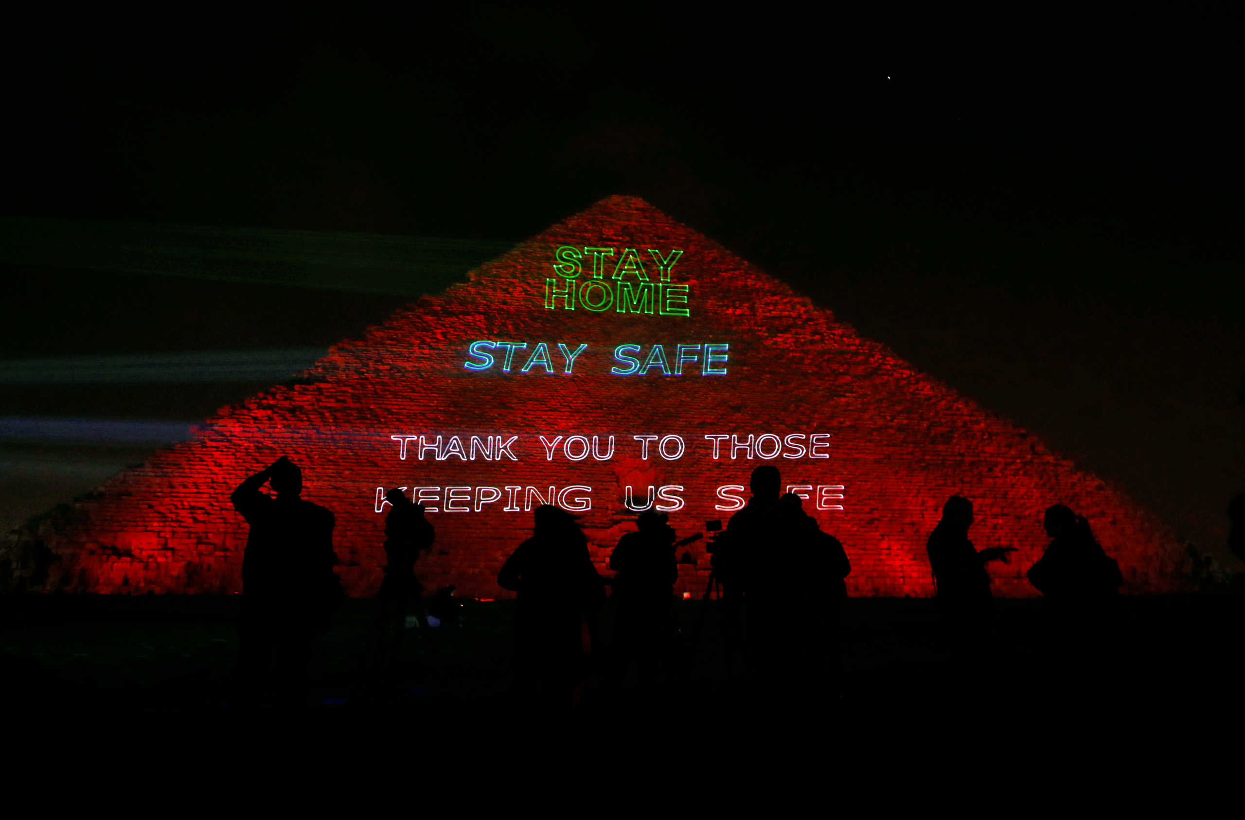 People are seen in front of the pyramid of Khufu, the largest of the Giza pyramid complex, illuminated with text encouraging to stay home, as Egypt ramps up its efforts to slow down the spread of coronavirus disease (COVID-19) outbreak, in Giza, on the outskirts of Cairo, Egypt, March 30, 2020. REUTERS