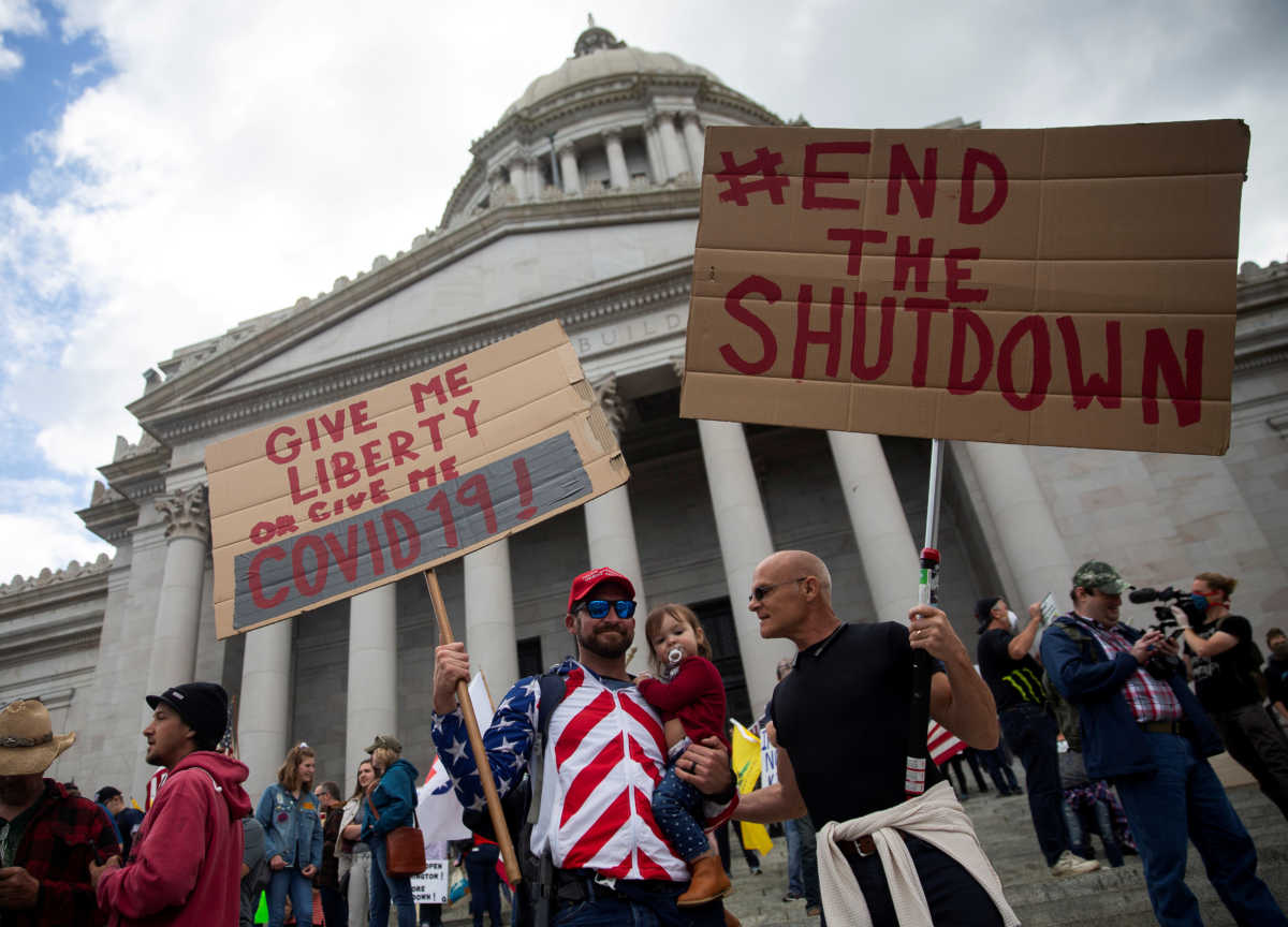 Two men hold signs as they protest against the state's extended stay-at-home order to help slow the spread of the coronavirus disease (COVID-19) as hundreds gather to demonstrate at the Capitol building in Olympia, Washington, U.S. April 19, 2020. REUTERS