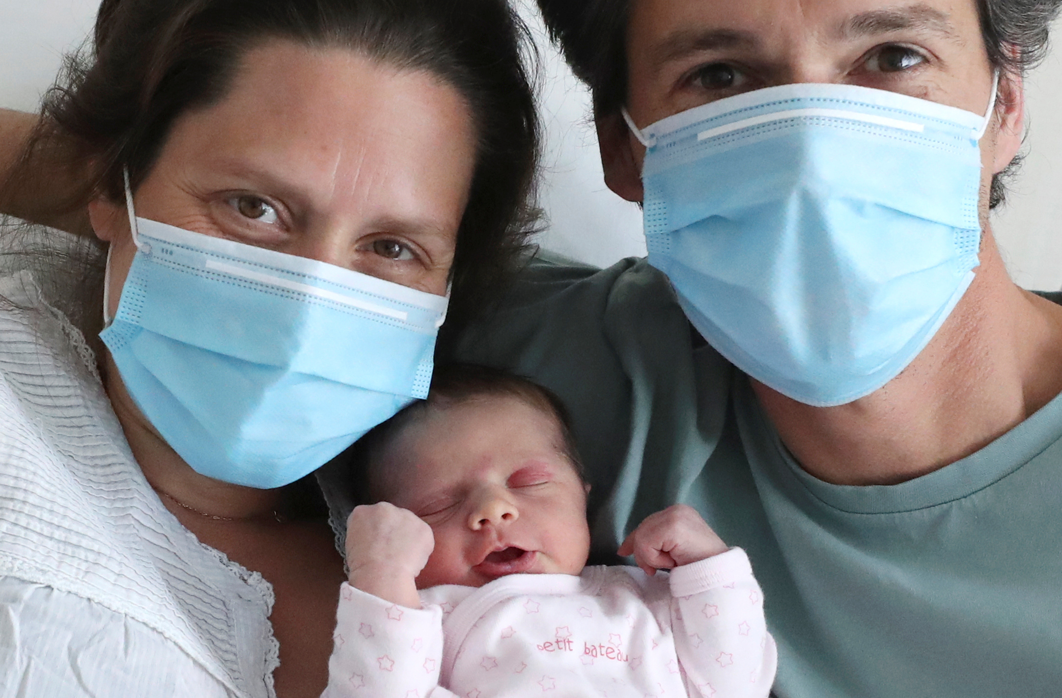 Amandine, who tested positive for the coronavirus disease (COVID-19) just before giving birth, and Francois, wearing protective face masks, are pictured with their newborn daughter Mahaut at the maternity at CHIREC Delta Hospital in Brussels, Belgium April 25, 2020.  REUTERS