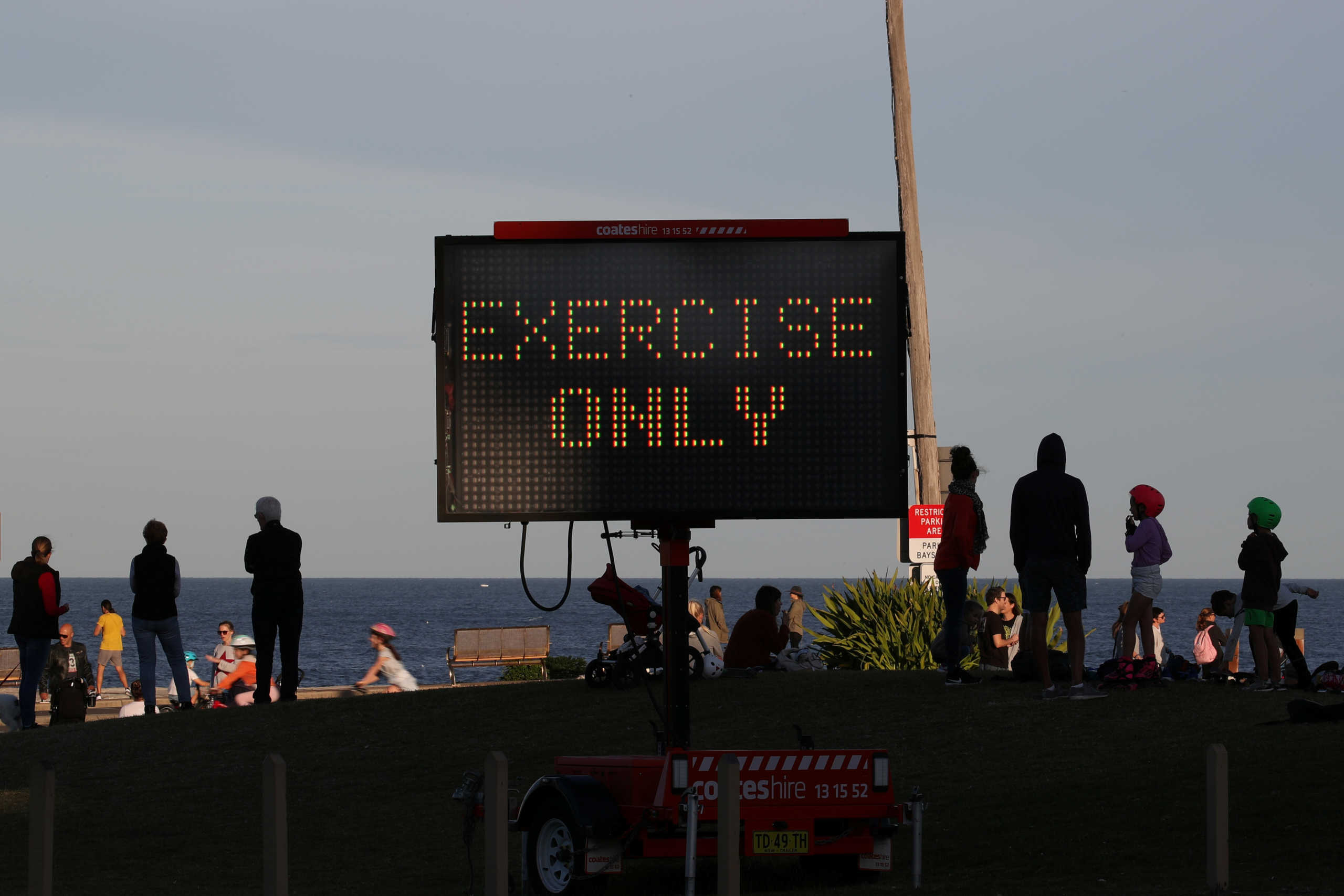 Families enjoying a clear evening on the coast stand near a sign reminding people of outdoor limitations amidst the easing of restrictions implemented to curb the spread of the coronavirus disease (COVID-19) in Sydney, Australia, May 6, 2020.  REUTERS